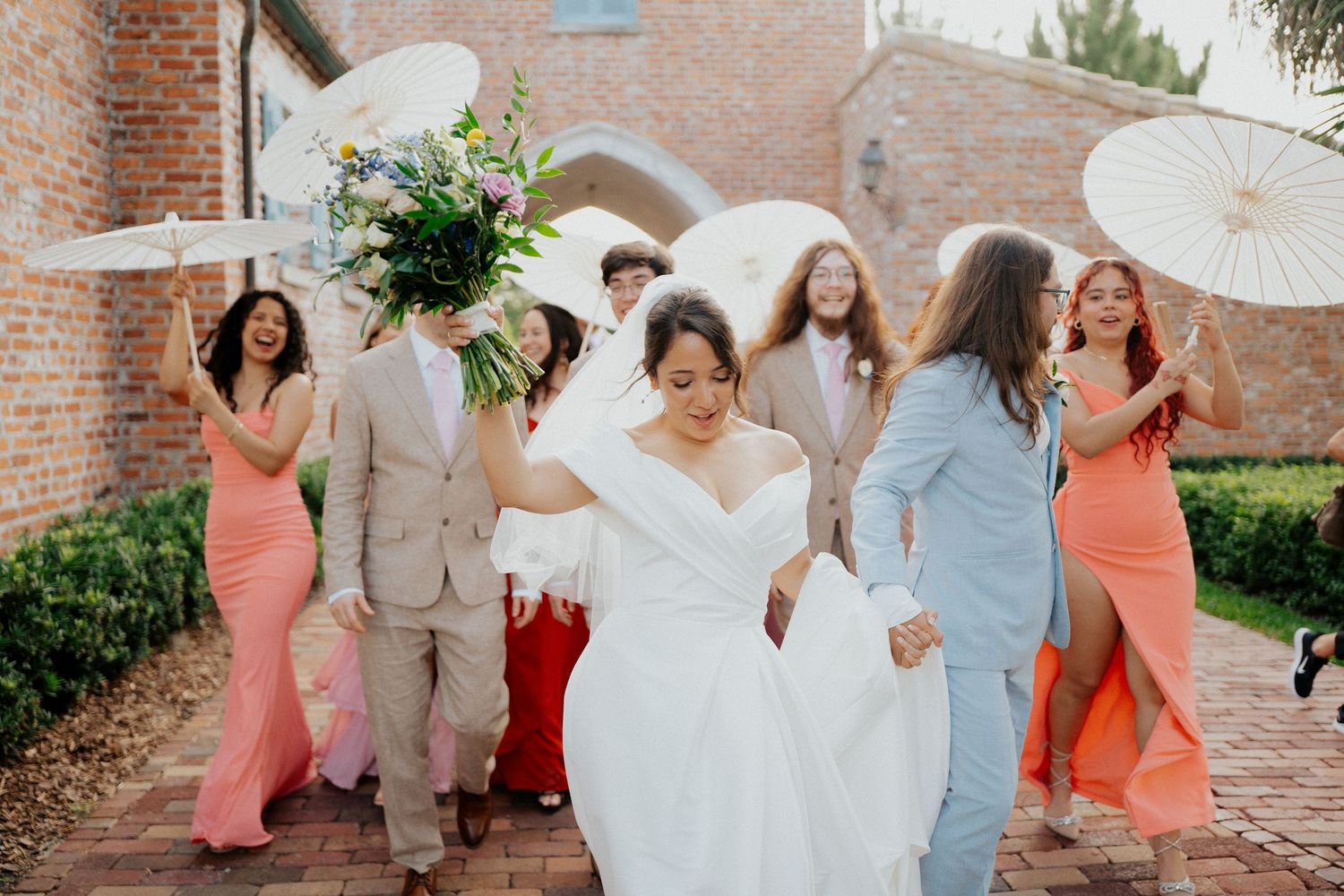 Wedding party celebrates with joyful expressions and poses against a rustic brick wall backdrop.