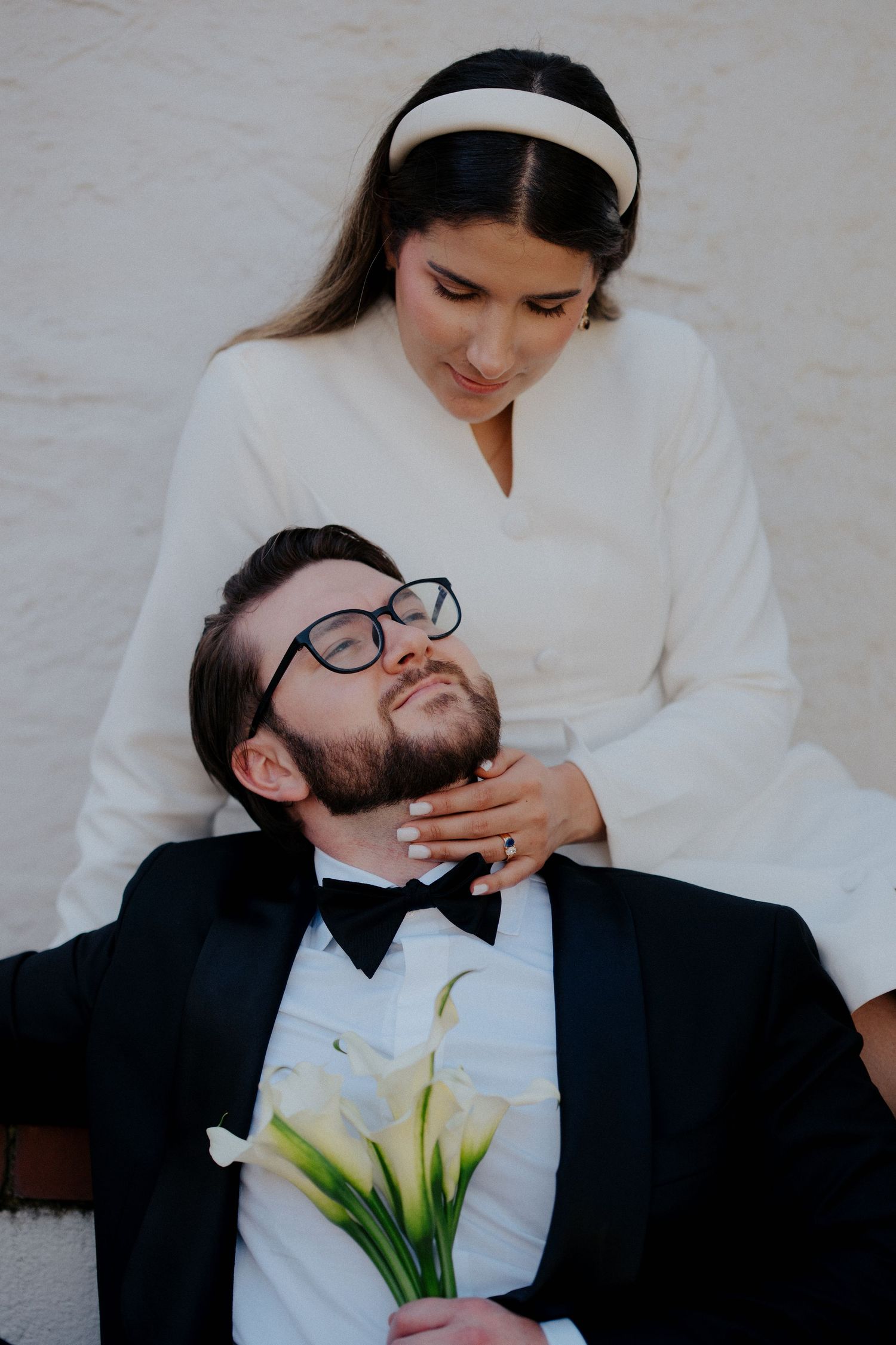 Intimate wedding portrait with calla lily bouquet and formal attire against white background.