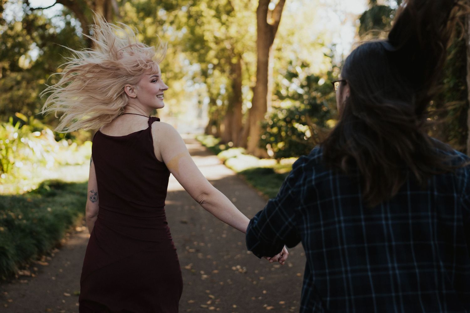 Two people dancing energetically on a forest path with sunlight filtering through trees.
