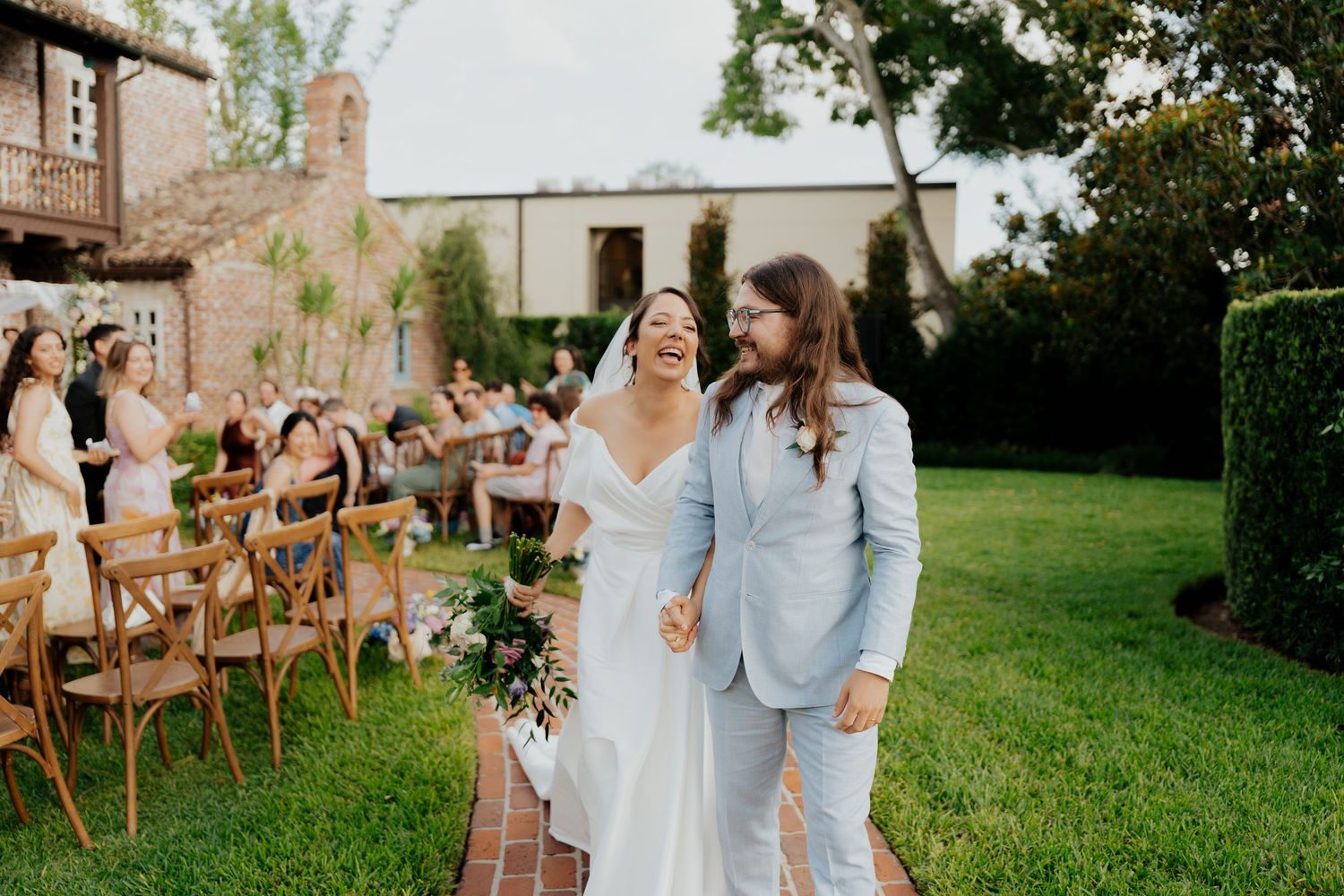 Outdoor wedding ceremony setup with wooden chairs and floral arrangements on a lush green lawn.