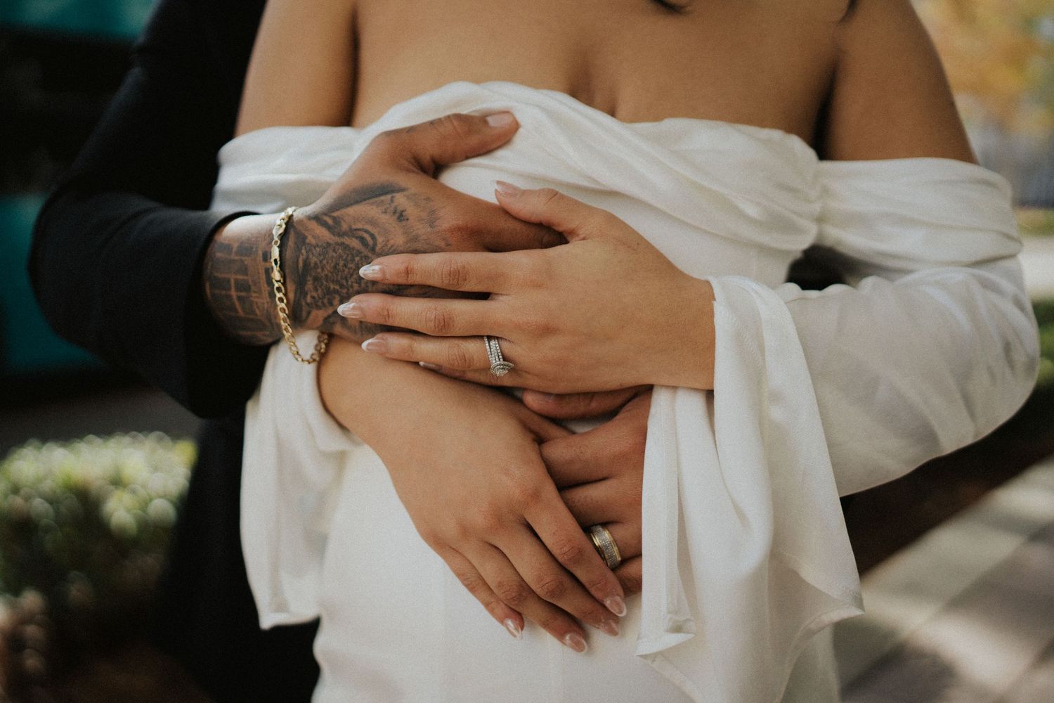 Close-up of intertwined hands showing wedding rings and formal attire.