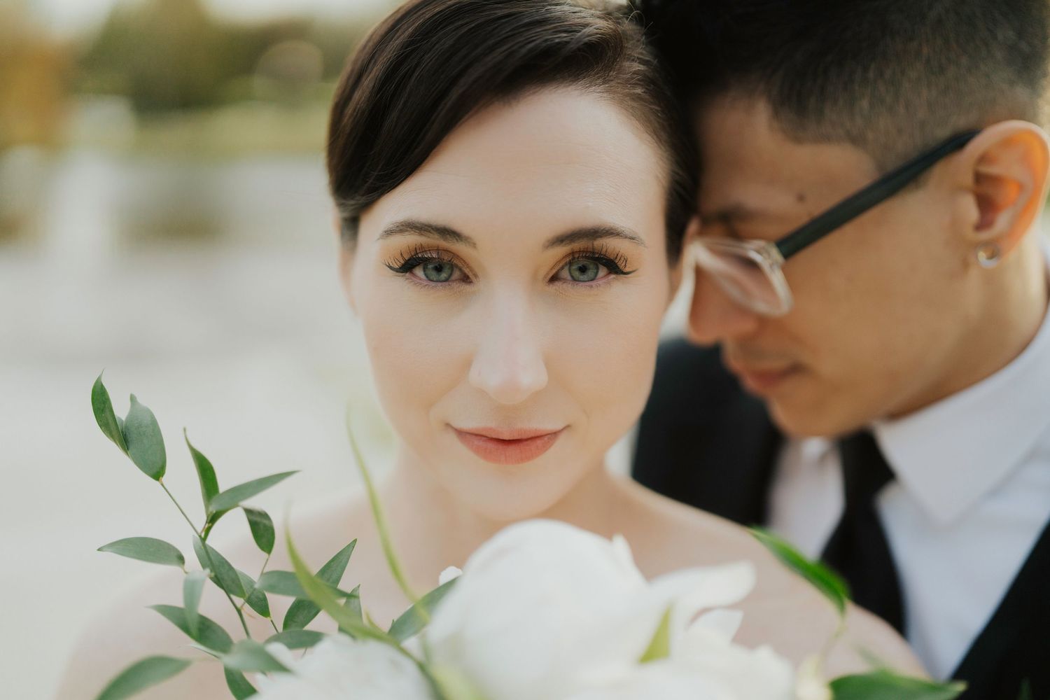 A romantic wedding portrait of a couple embracing outdoors with soft natural lighting and greenery in the background.