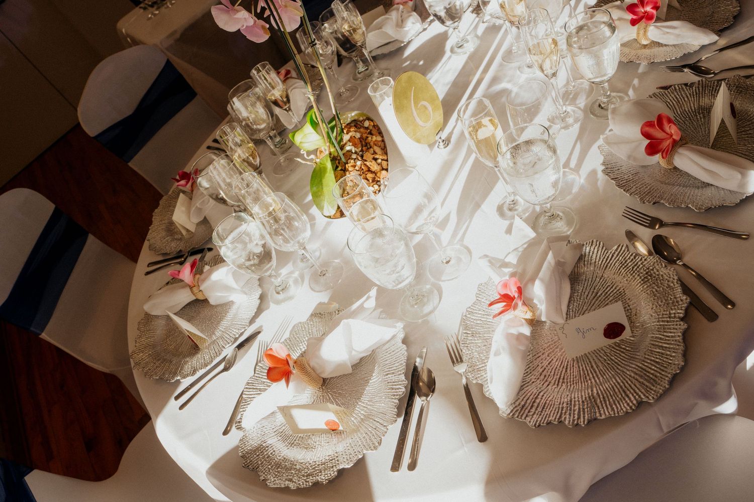 Elegant wedding reception table setting with white linens, crystal glassware, floral centerpieces, and decorative charger plates.