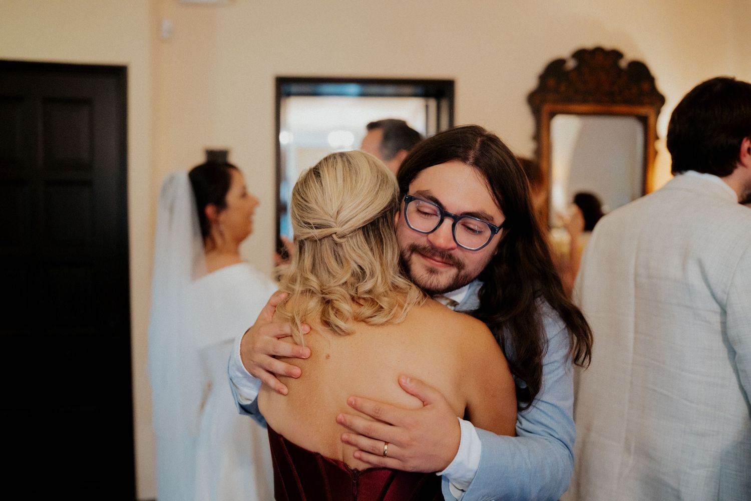 Guests share emotional embraces during a wedding reception in a warmly lit indoor venue.