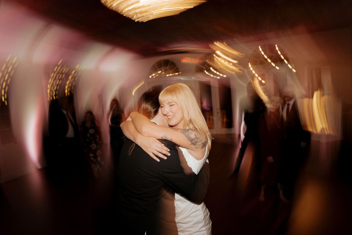 Couple embracing and dancing joyfully at a wedding reception with warm bokeh lights in the background.
