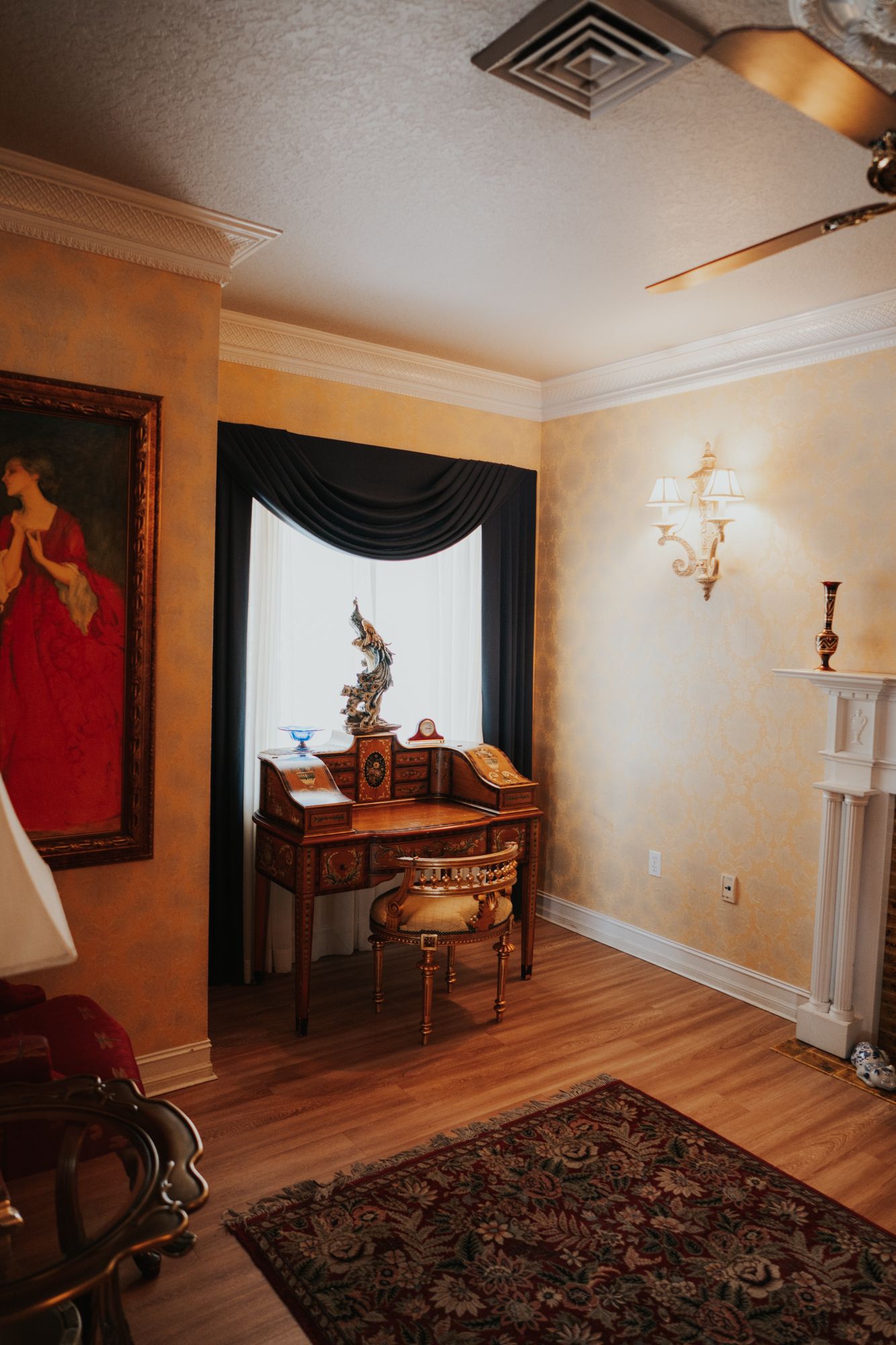 Antique writing desk and classical artwork in a room with warm peach walls and hardwood flooring.
