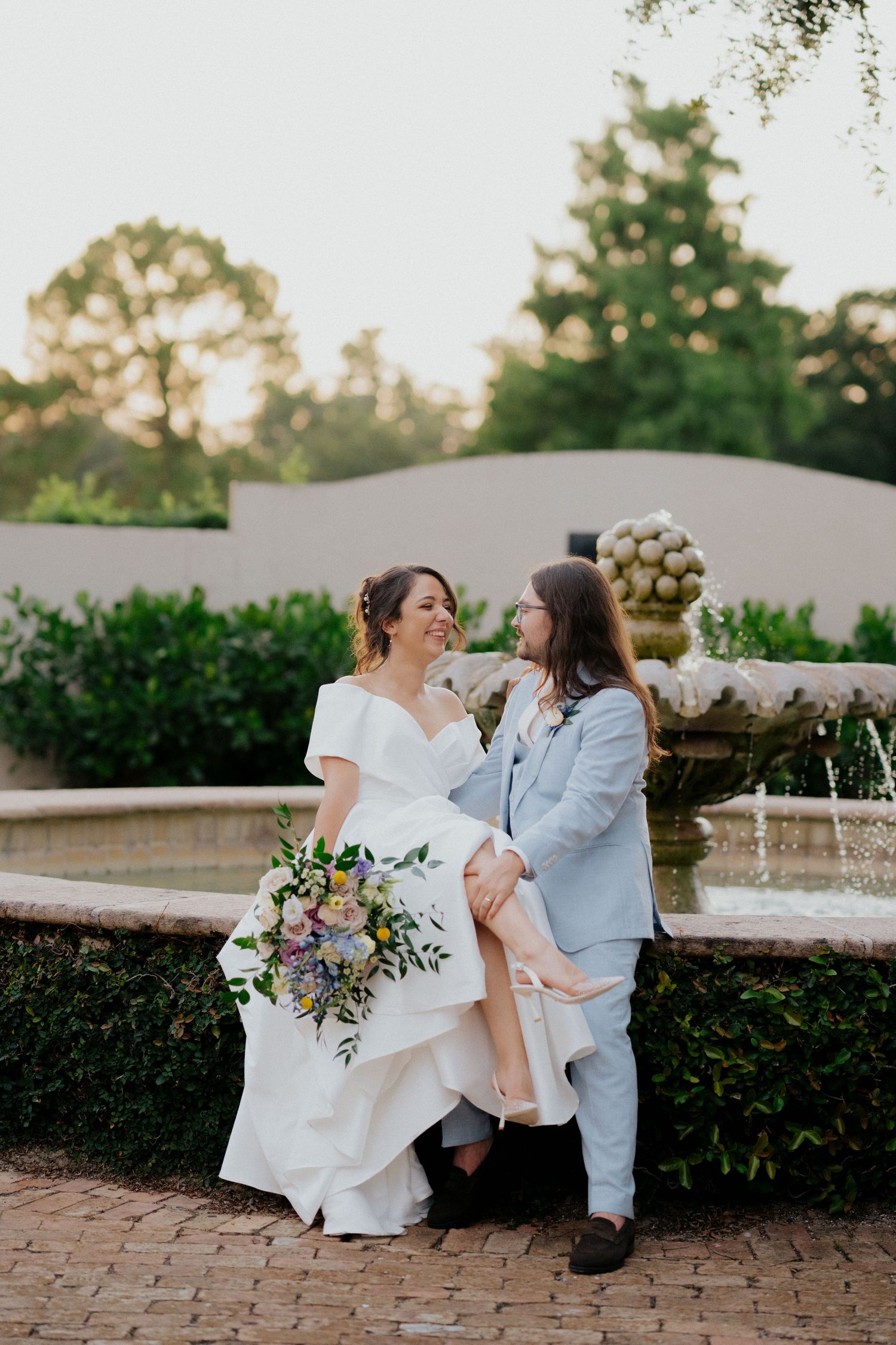 A couple dips and dances romantically on a brick patio with a flowing white dress and blue suit.