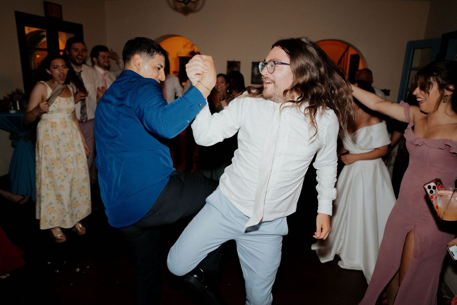 Couples dancing together at a wedding reception in a dimly lit venue with warm lighting.
