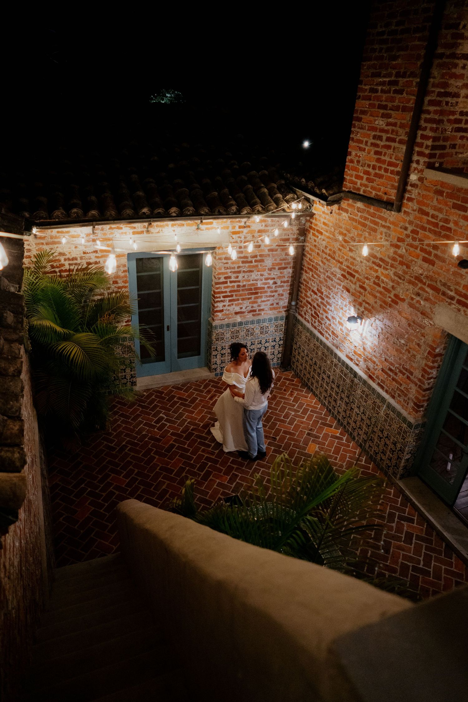 String lights illuminate a brick exterior walkway at night creating an ambient glow along the path.