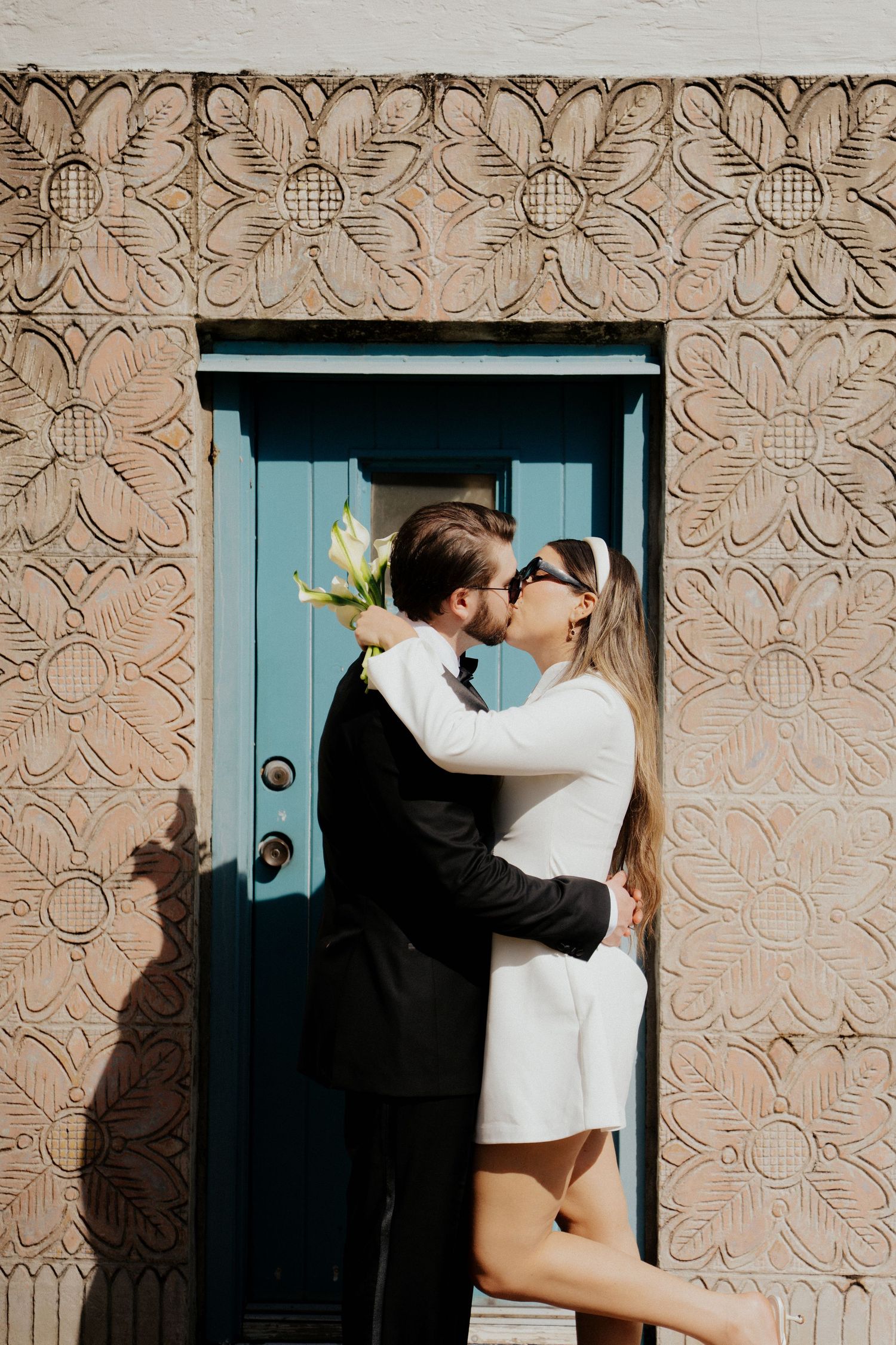 A romantic moment captured in front of a turquoise door with ornate textured wall patterns in the background.