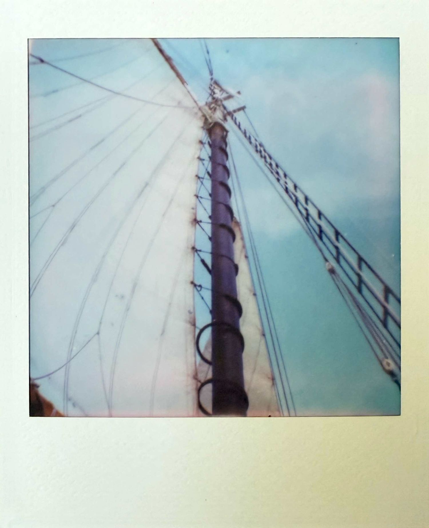 Looking up at tall sailing ship mast with rigging and ropes against blue sky, vintage Polaroid.