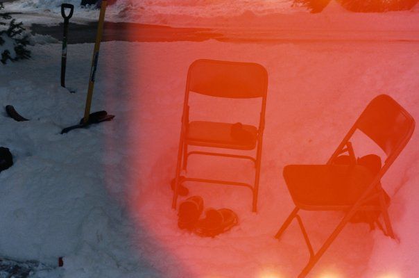 Red light-exposed photo of folding chairs and shovels in snow-covered backyard during winter.