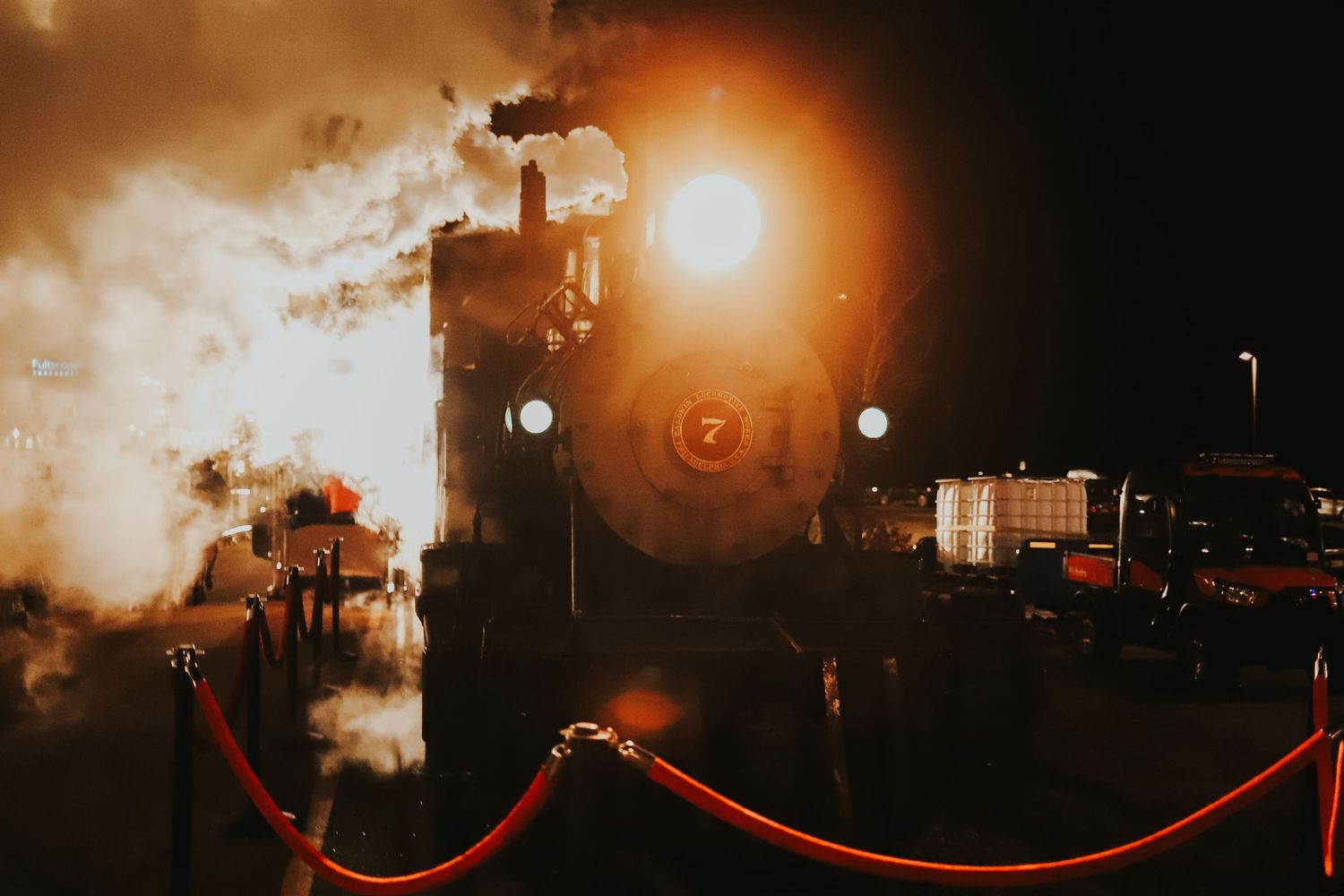 Vintage steam locomotive engine illuminated at night with glowing headlight and billowing smoke.