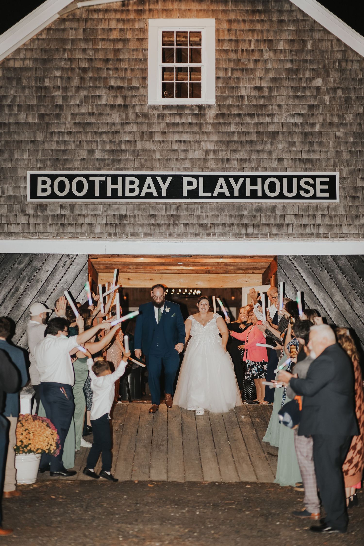 A newlywed couple exits the Boothbay Playhouse barn amid cheering wedding guests.
