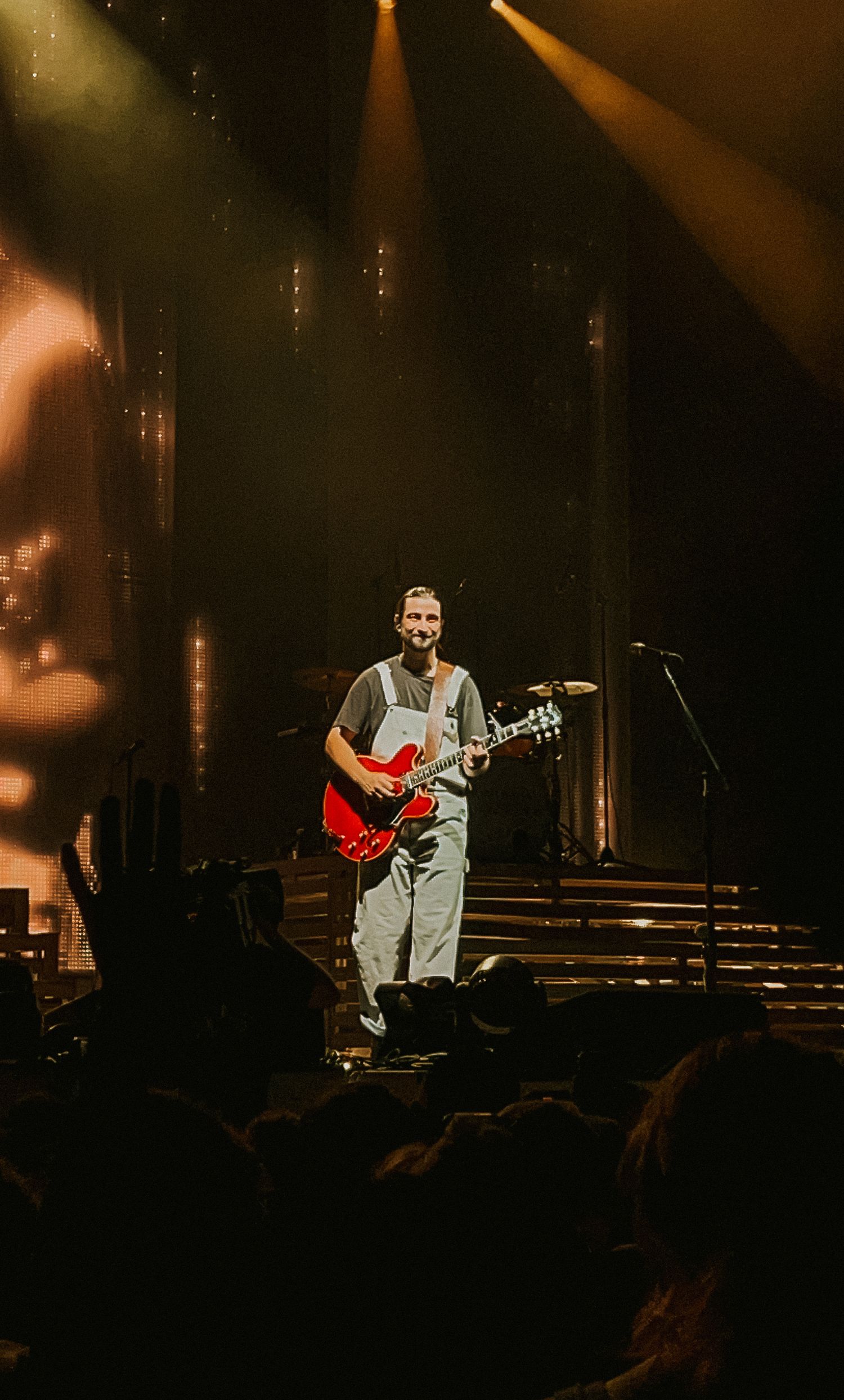 Male guitarist performing on stage with red electric guitar under dramatic concert stage lighting.