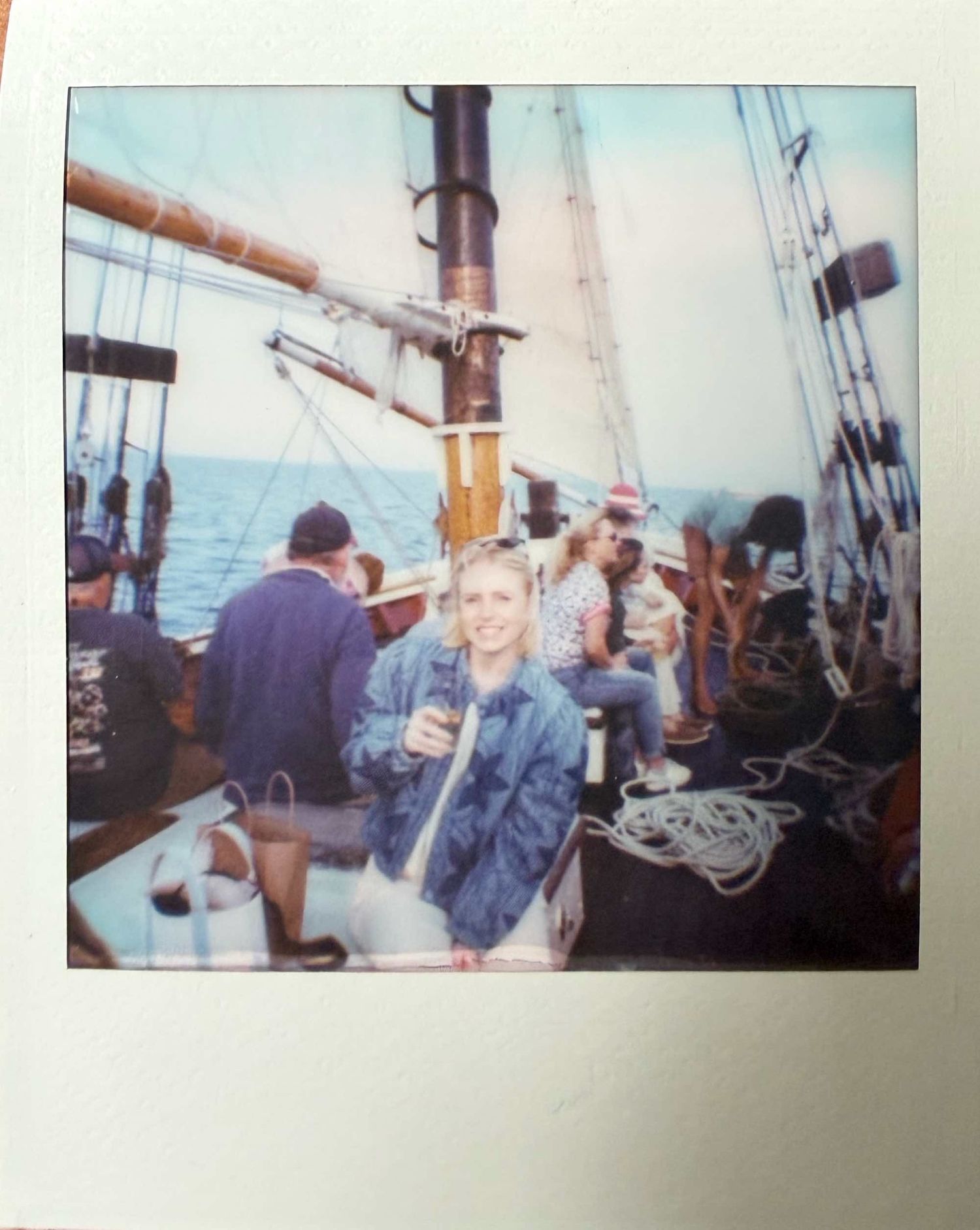 Woman smiling on deck of sailing schooner with other passengers and rigging visible, vintage Polaroid.