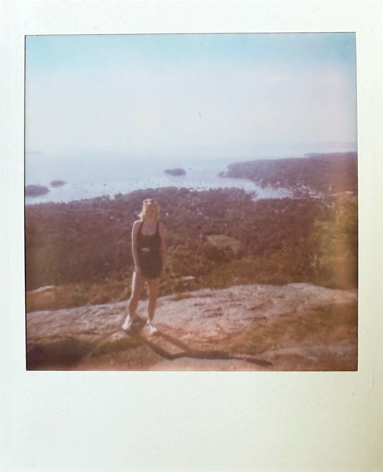 Person standing on rocky coastal overlook gazing at ocean view, Polaroid photo.