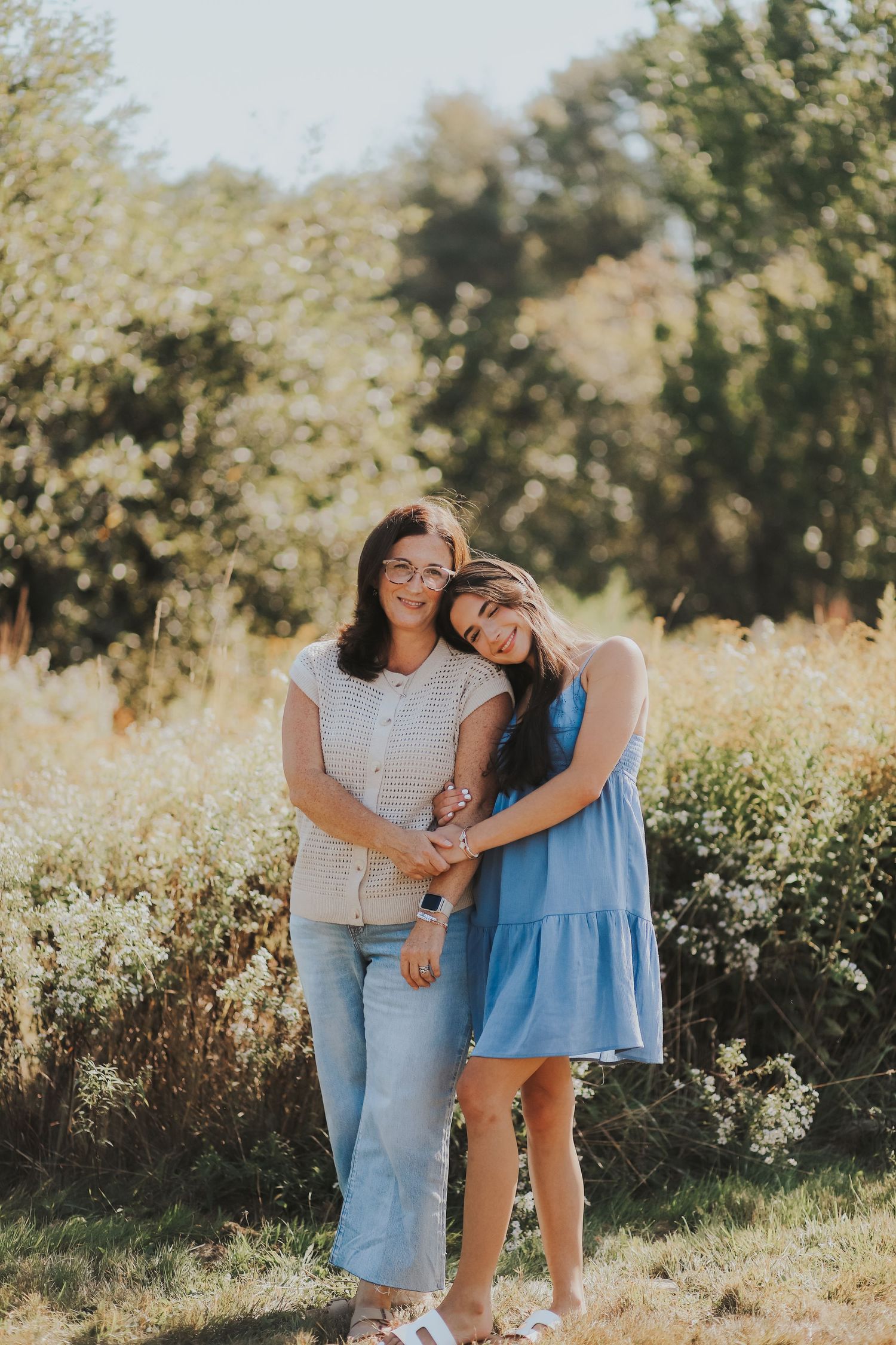 Mother and teenage daughter embracing and smiling together in a sunny outdoor field setting.