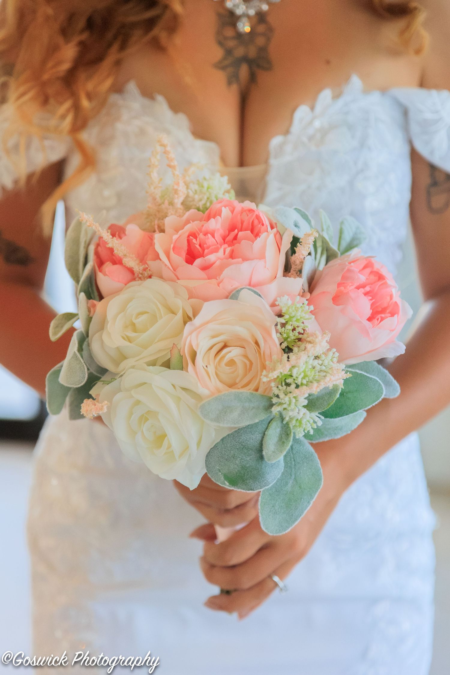 Close-up of bridal bouquet featuring coral peonies, cream roses, and sage green succulents held by bride.