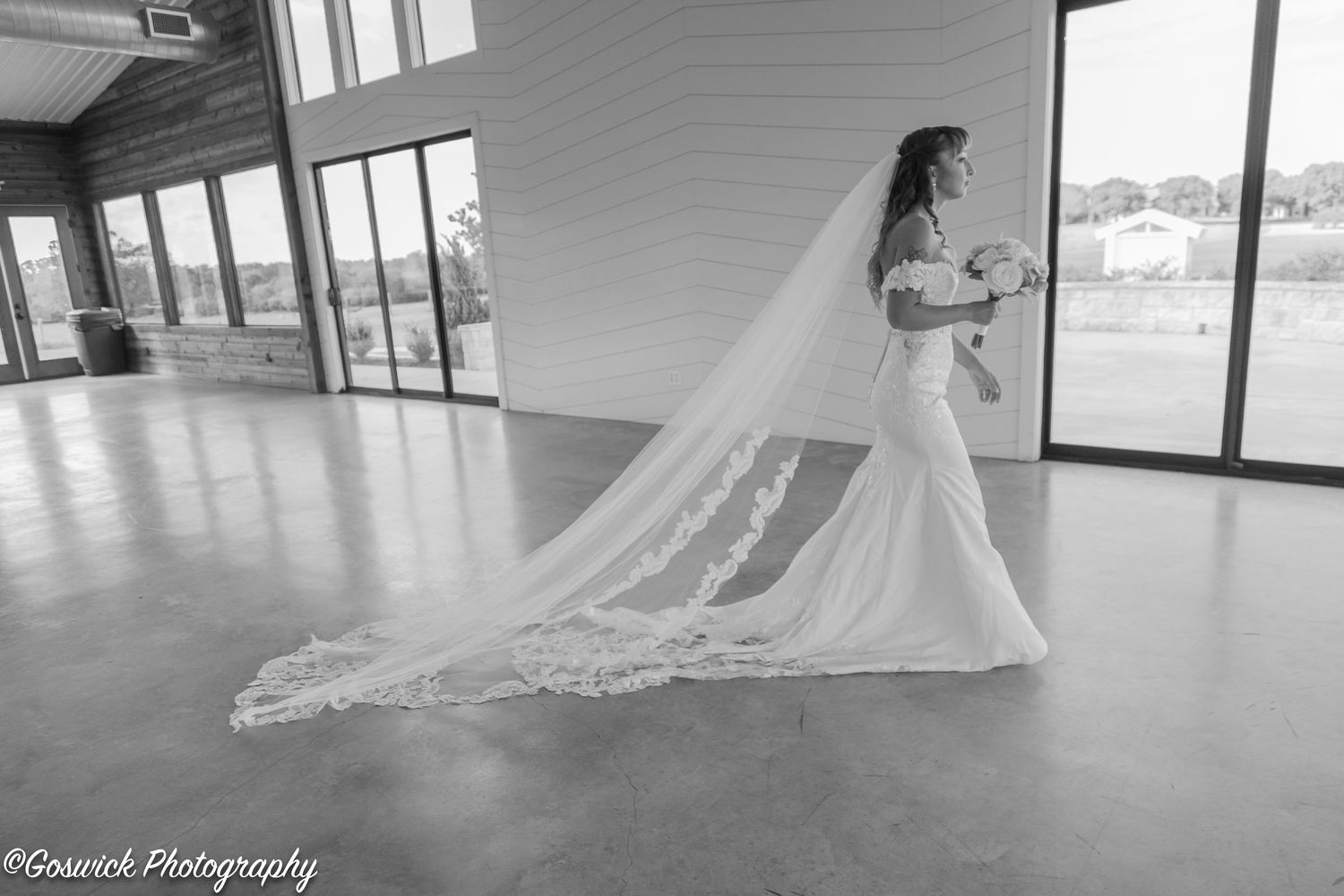 Black and white bridal portrait of bride in mermaid gown with dramatic lace cathedral veil in barn venue.