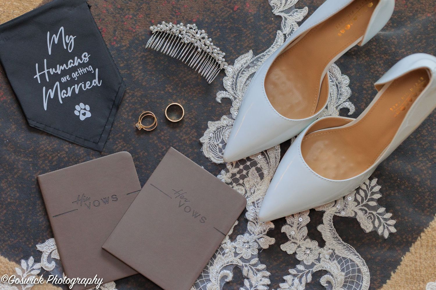 Wedding flat lay featuring white heels, rings, vow booklets, hair comb, and a dog bandana.