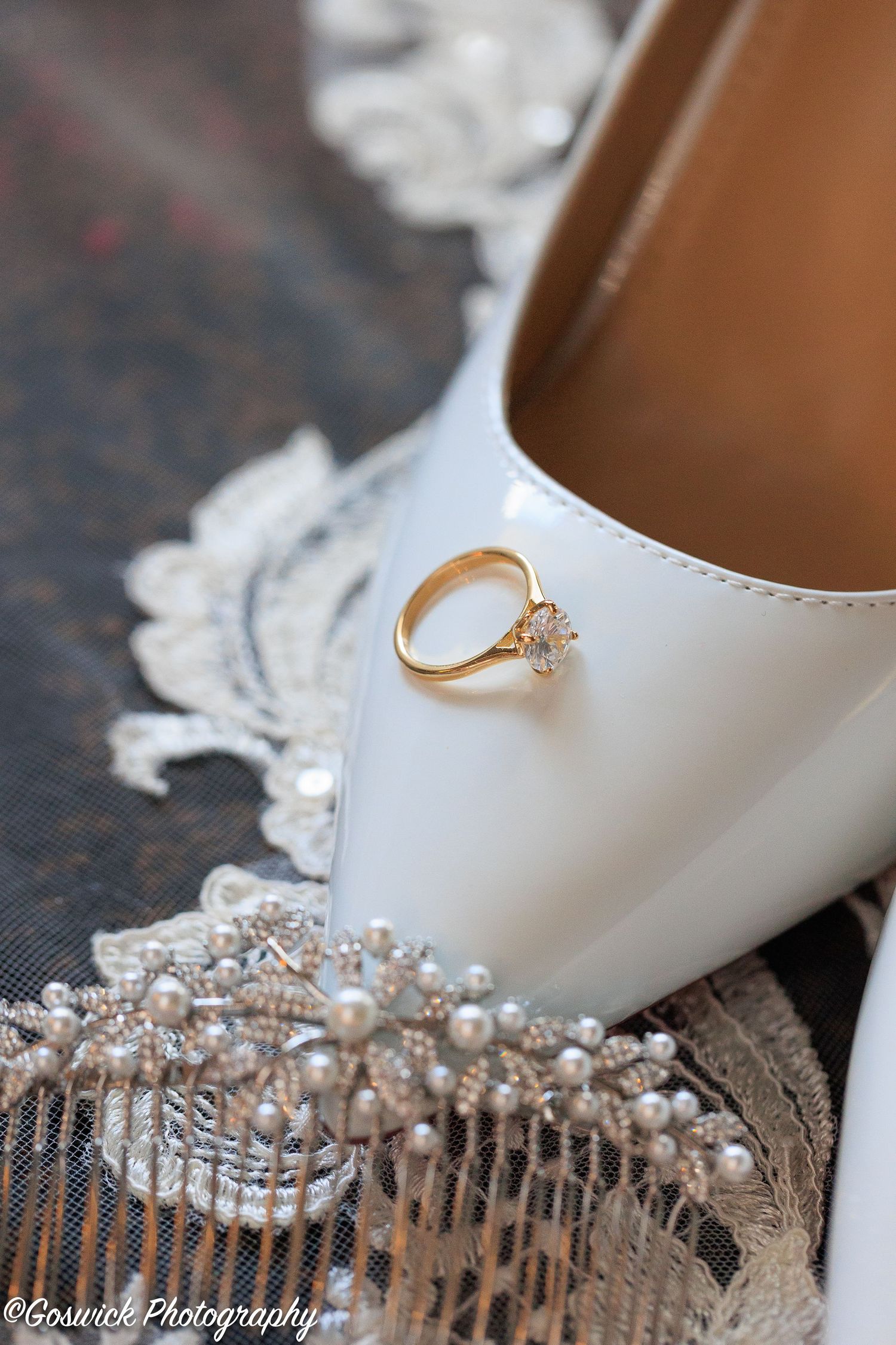 Gold diamond engagement ring resting on white bridal heel with pearl lace detail.