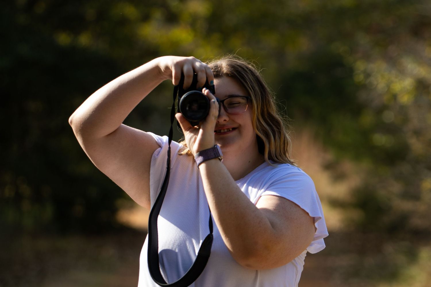 Young woman photographer smiling while taking photos outdoors in natural light.