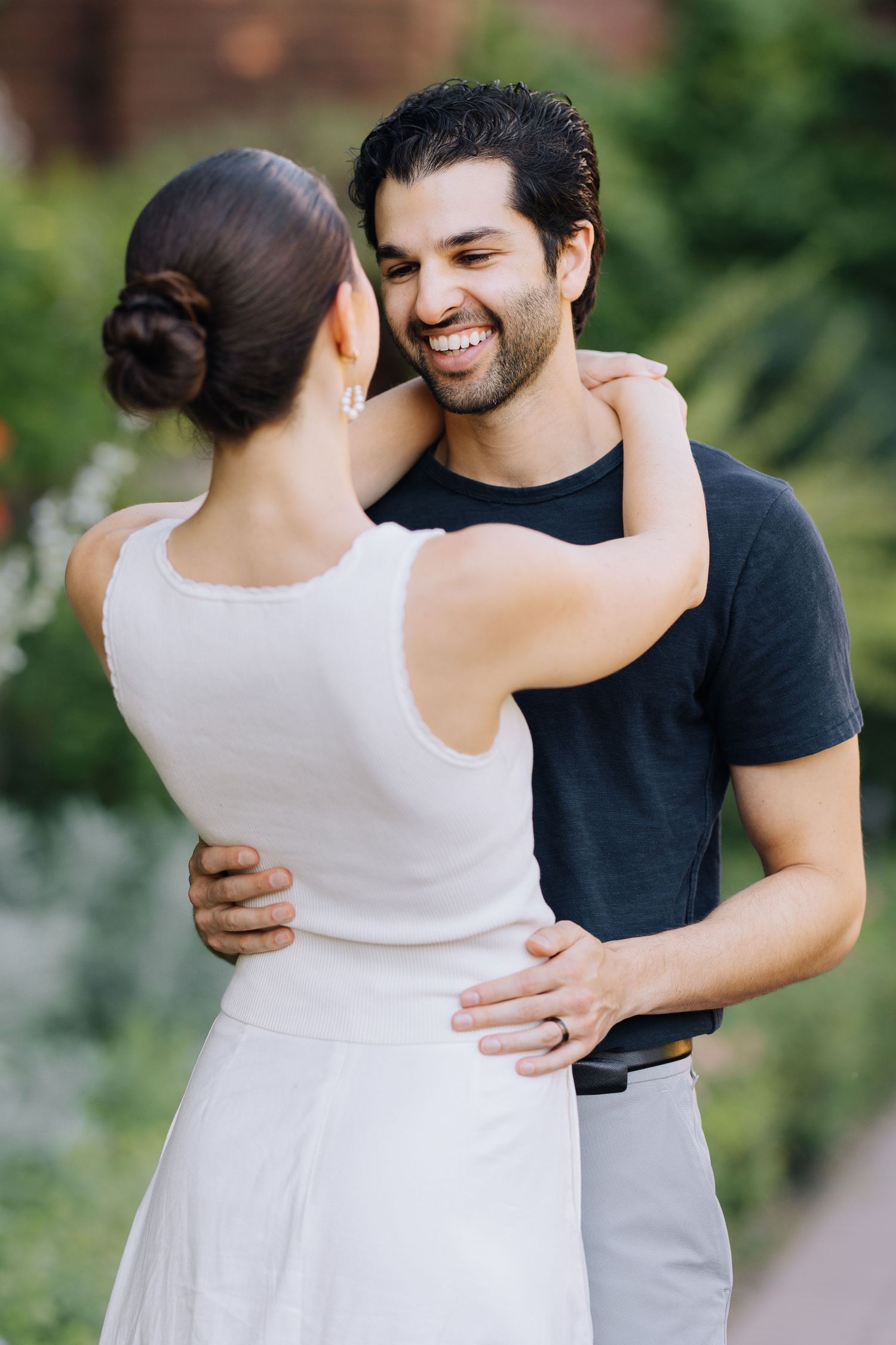 Smiling man in black shirt embracing woman in white dress in a lush garden setting during Filoli engagement photoshoot.