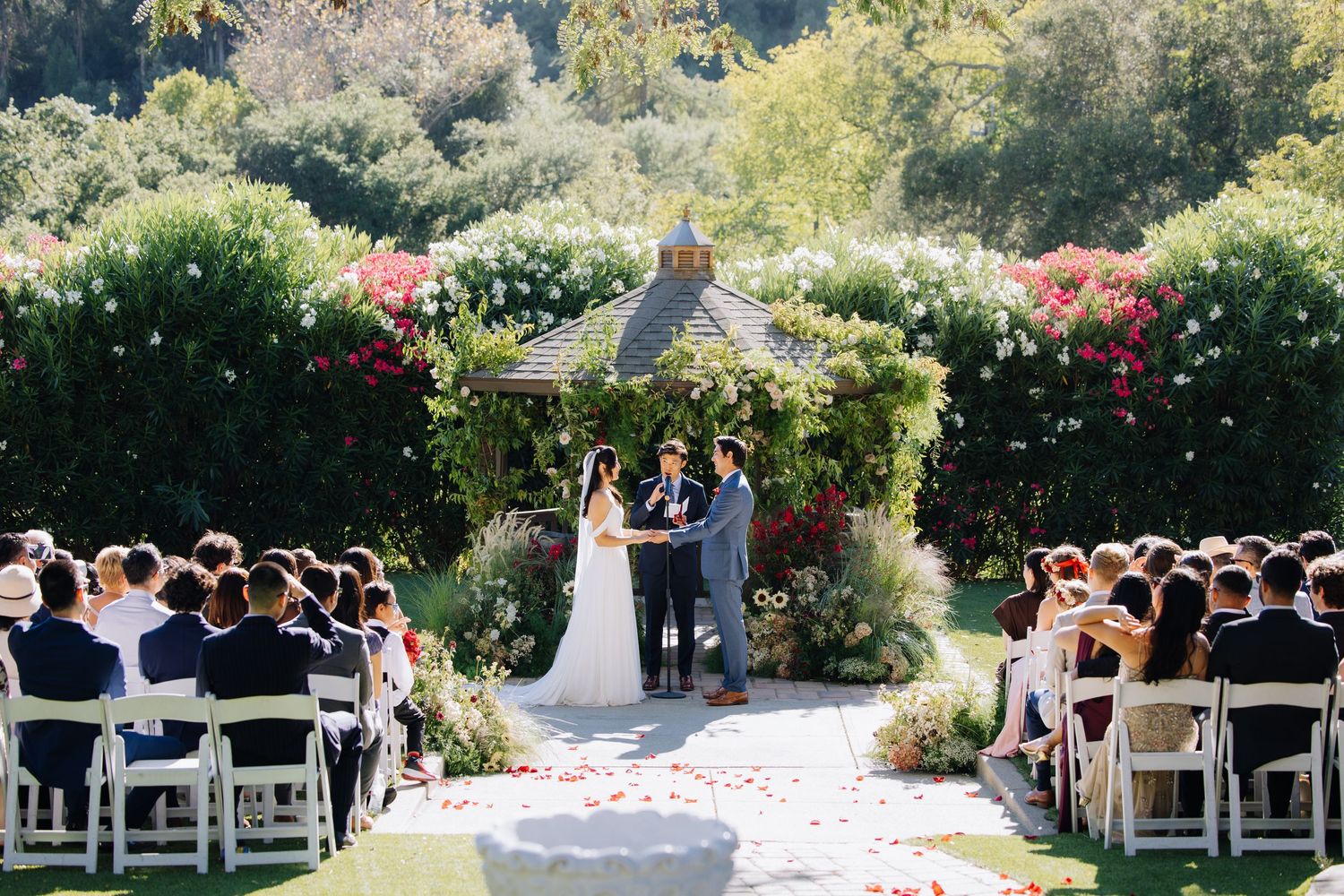 Romantic outdoor wedding ceremony under a floral gazebo with rose petal aisle and lush garden setting in Elliston Vineyards in Sunol, CA.