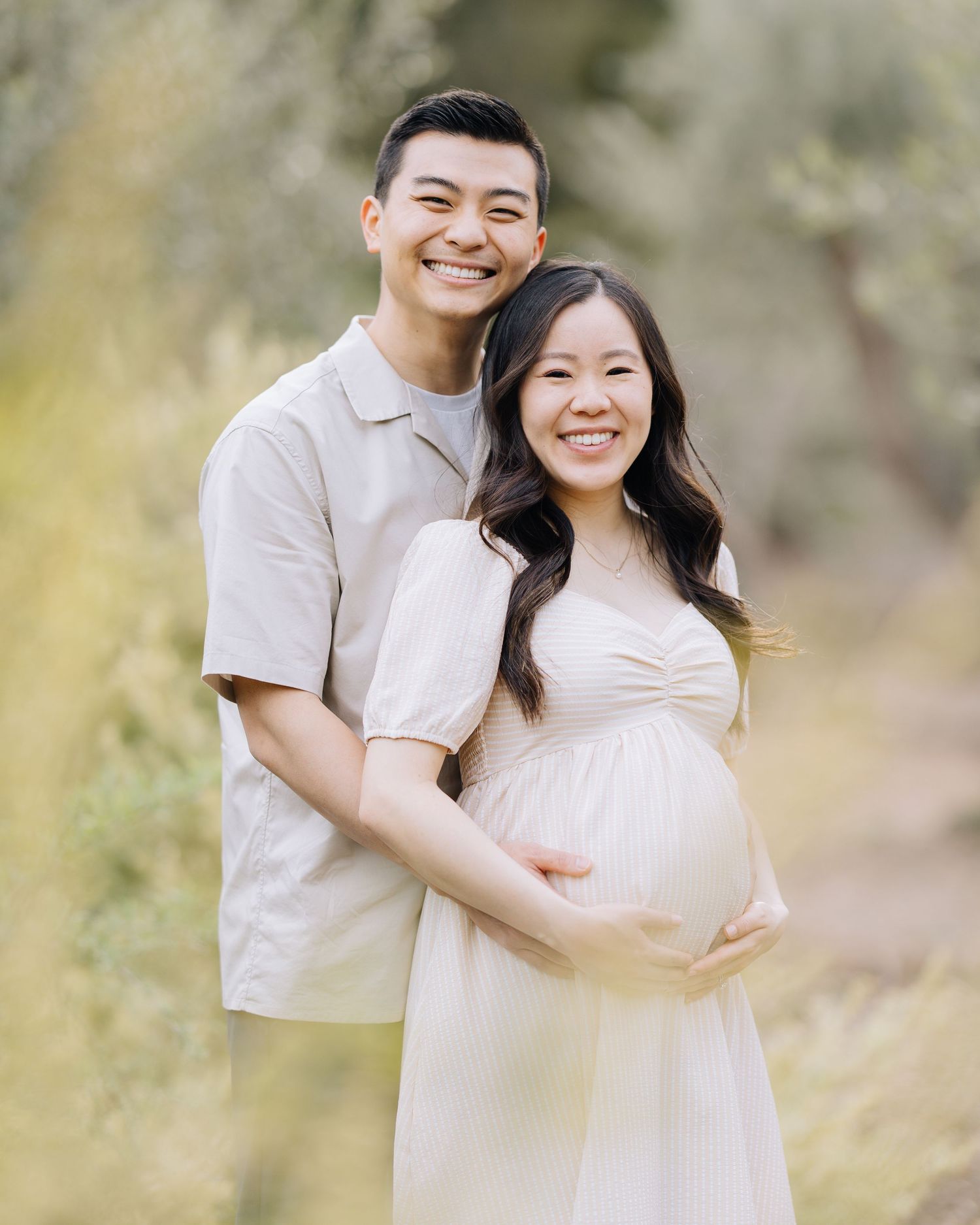 Happy pregnant couple posing together in a sun-drenched outdoor setting, woman in white maternity dress at Filoli Woodside maternity session