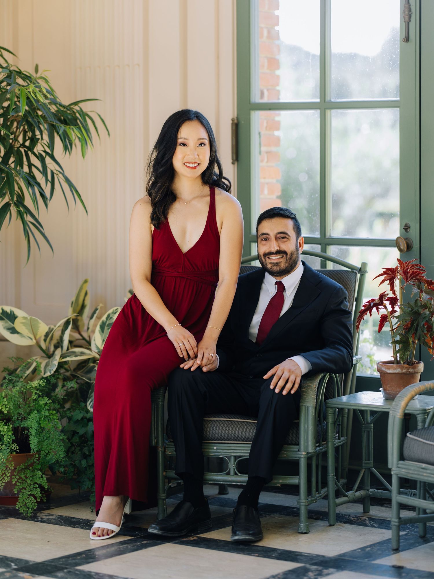 Elegant couple in matching red and black formal attire seated together on a garden porch during Filoli engagement photoshoot.