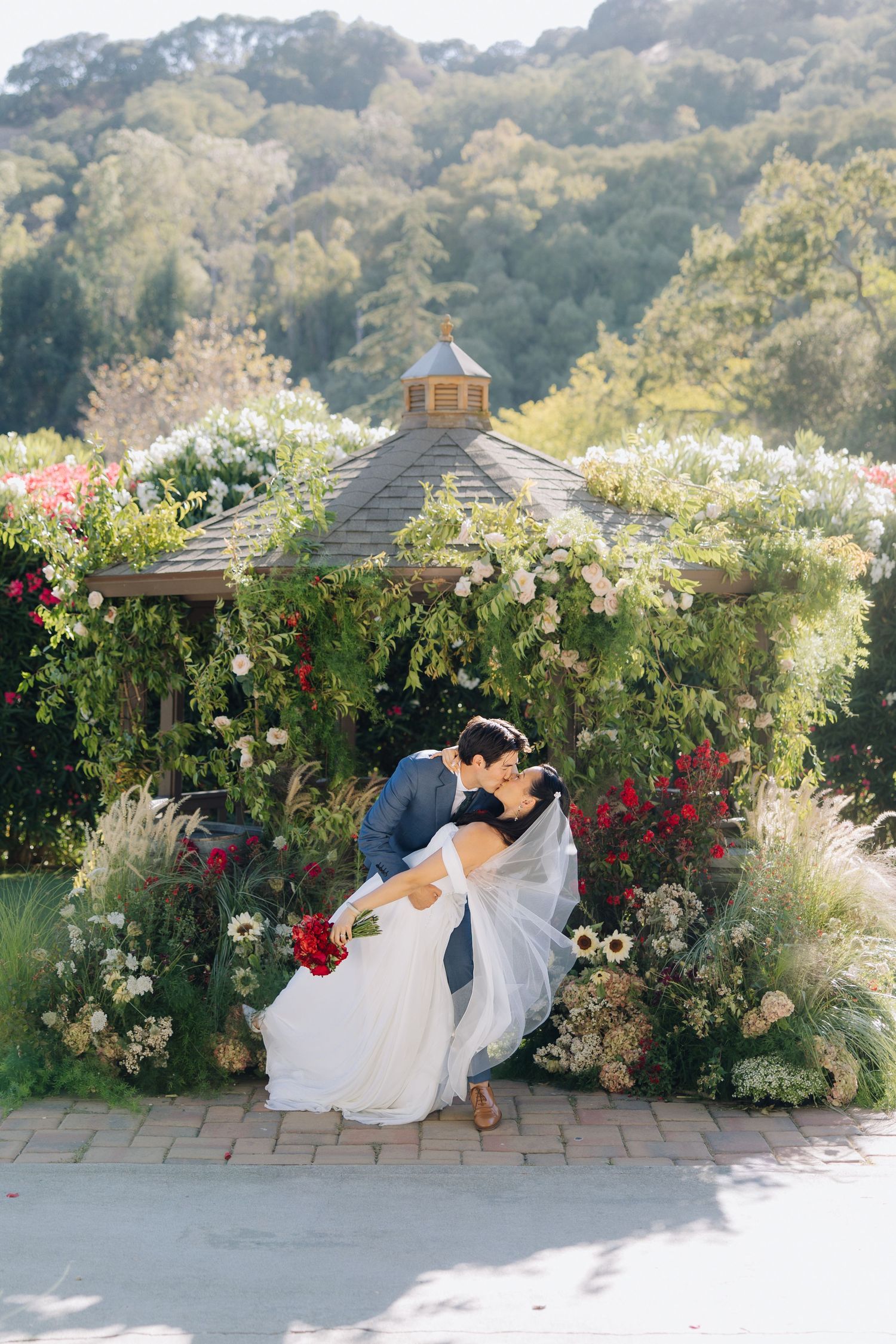 Bride and groom sharing romantic dip kiss under flower-covered gazebo in garden at Elliston Vineyards in Sunol, California