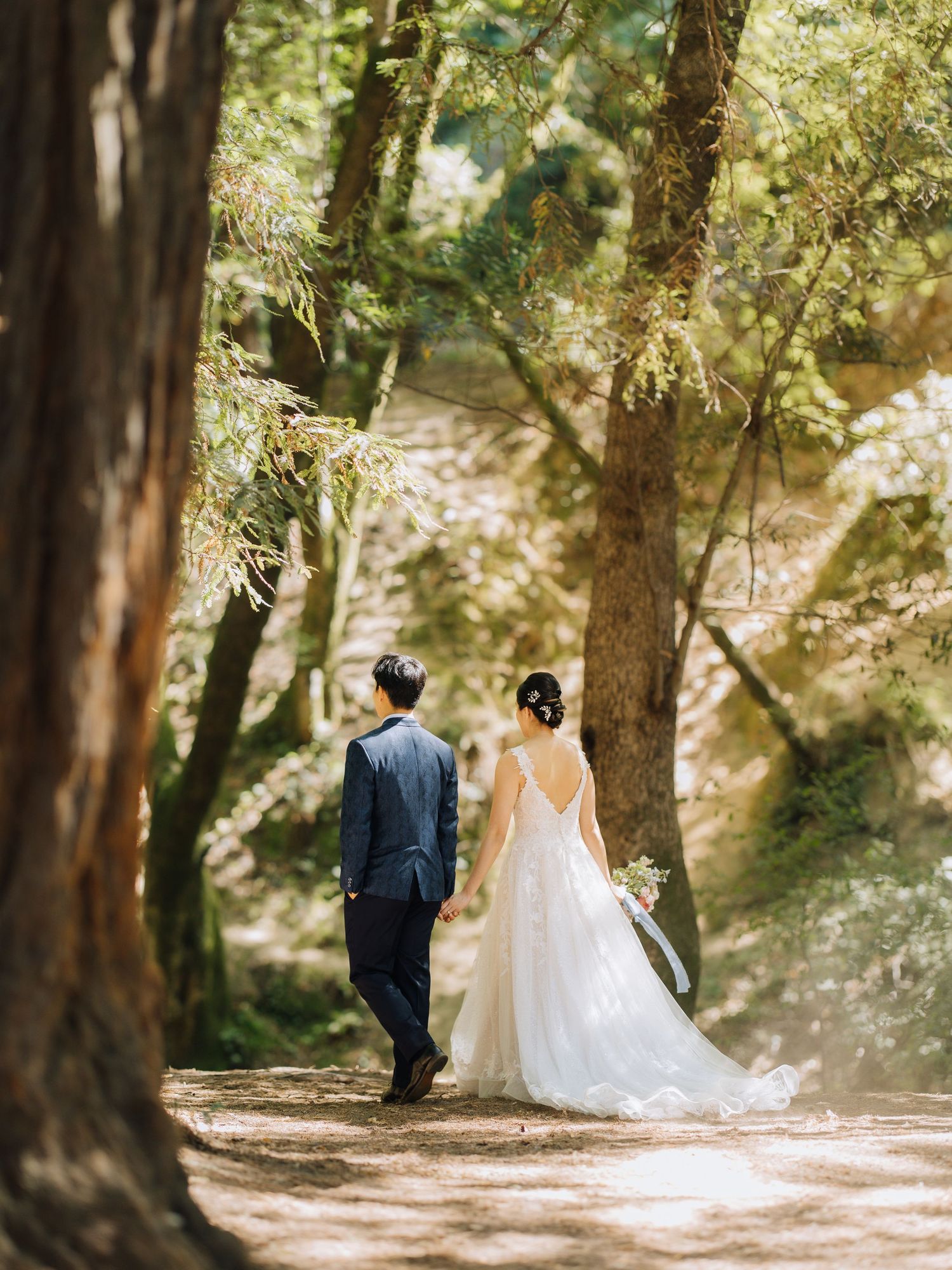 Bride and groom walking hand in hand through sunlit forest path on wedding day at Outdoor Art Club in Mill Valley, CA.