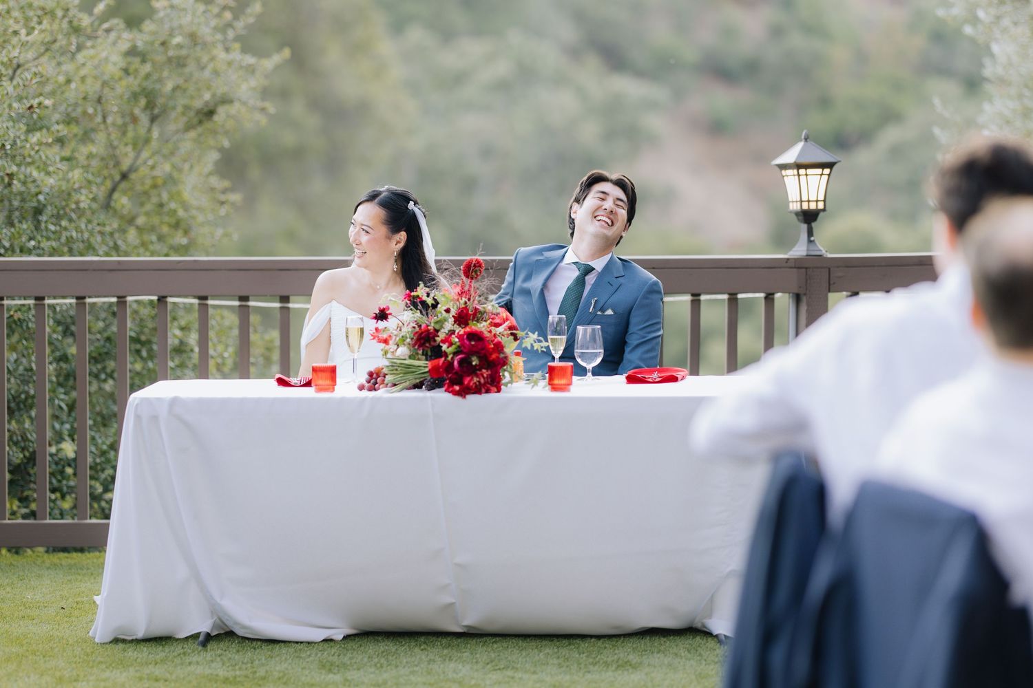 Bride and groom laughing joyfully at sweetheart table during outdoor wedding reception on a deck at Elliston Vineyards in Sunol.