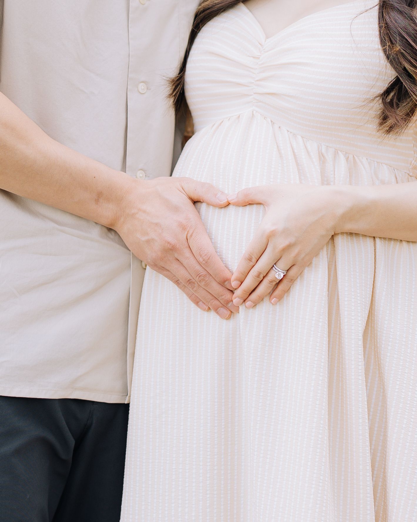 Couple forming a heart shape with their hands over a pregnant belly, woman wearing anengagement ring at Filoli Woodside maternity session.