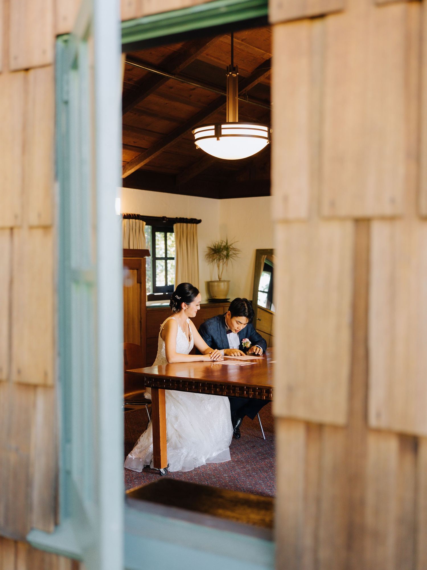 Bride and groom signing wedding documents at a wooden table in a rustic lodge at Outdoor Art Club in Mill Valley, CA.