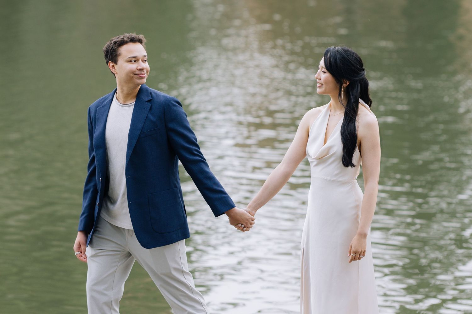 Happy couple holding hands by a serene lake during an outdoor engagement session in Palace of Fine Arts, SF.