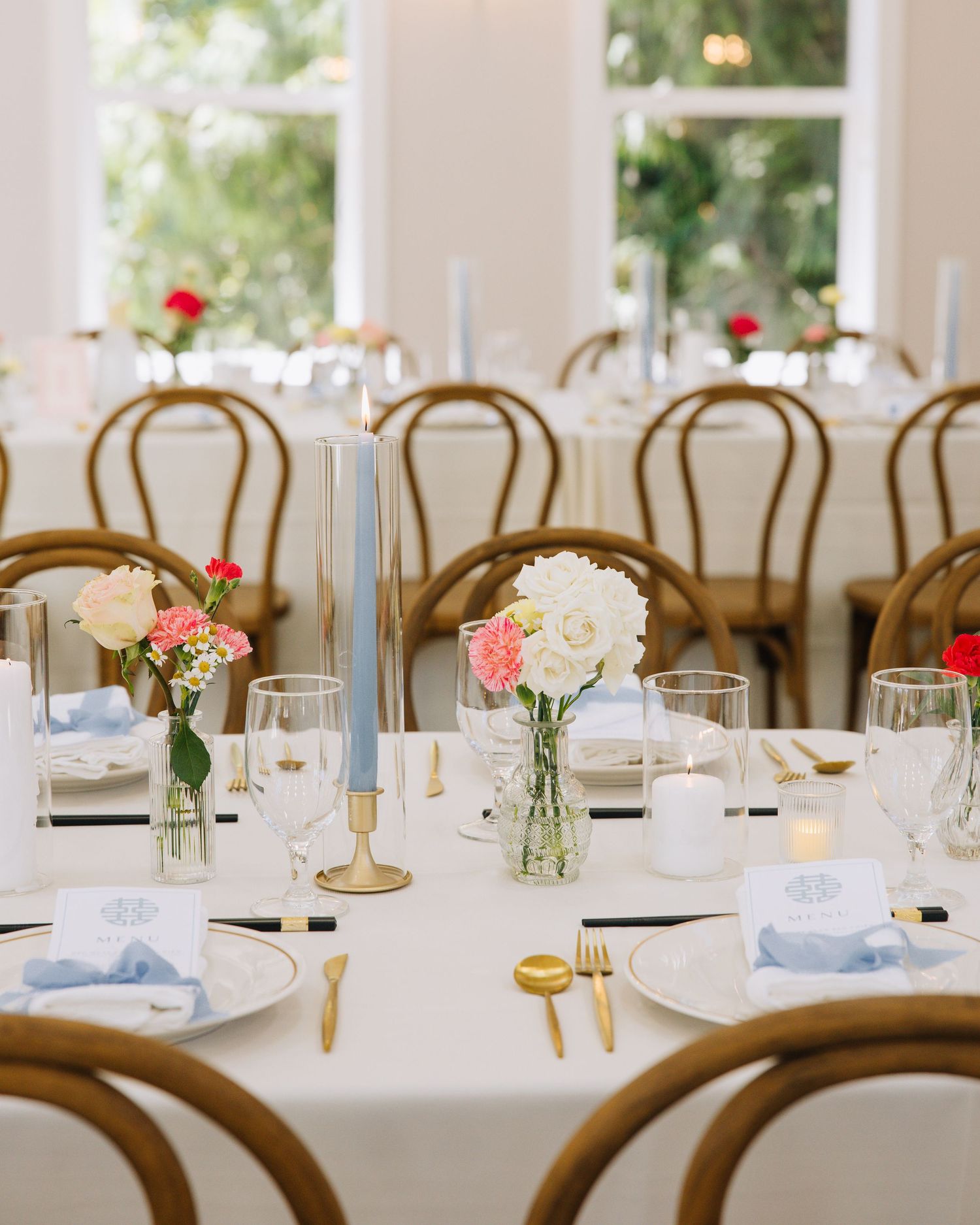 Round reception tables with white hydrangeas, pink carnations, blue taper candles, and gold flatware settings.