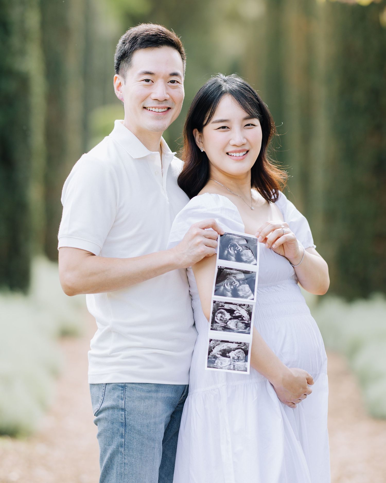 Smiling Asian couple holding ultrasound strip during outdoor maternity photography session at Filoli Woodside, CA.
