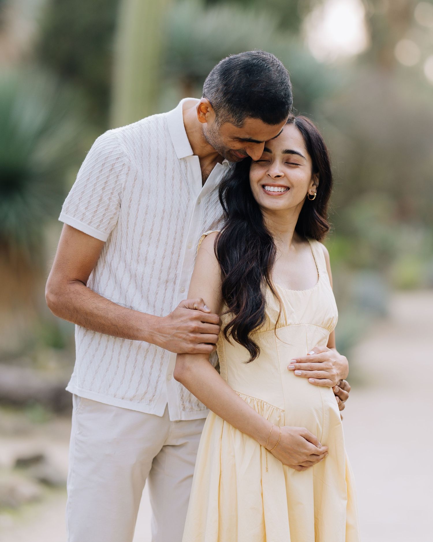Pregnant woman in yellow dress embraced by partner during outdoor maternity session at Stanford Arizona Garden.