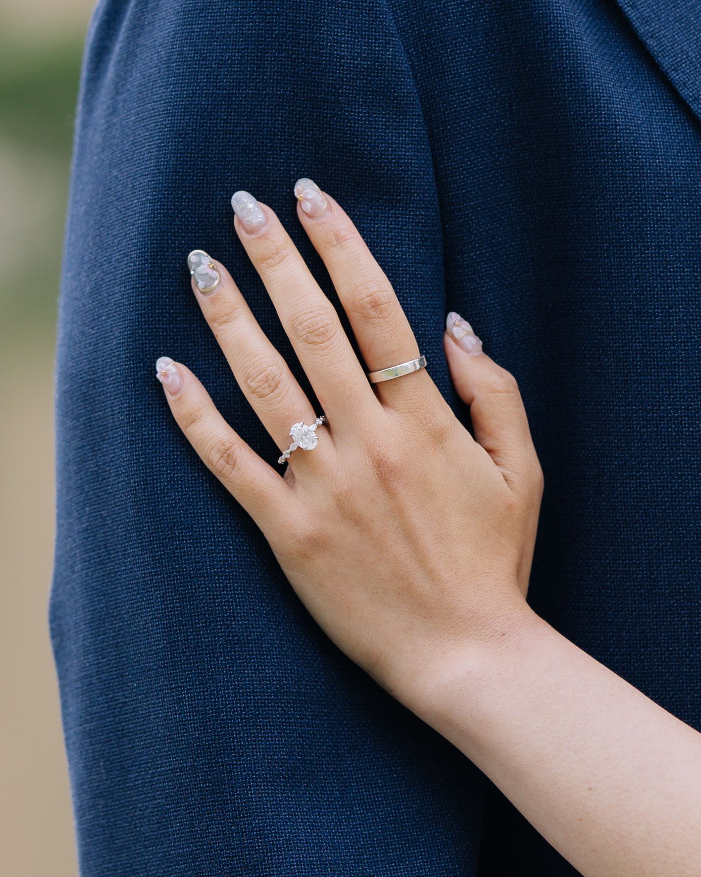 Close-up of an engagement ring on a woman's hand resting on a navy blue jacket sleeve during engagement photoshoot in SF.