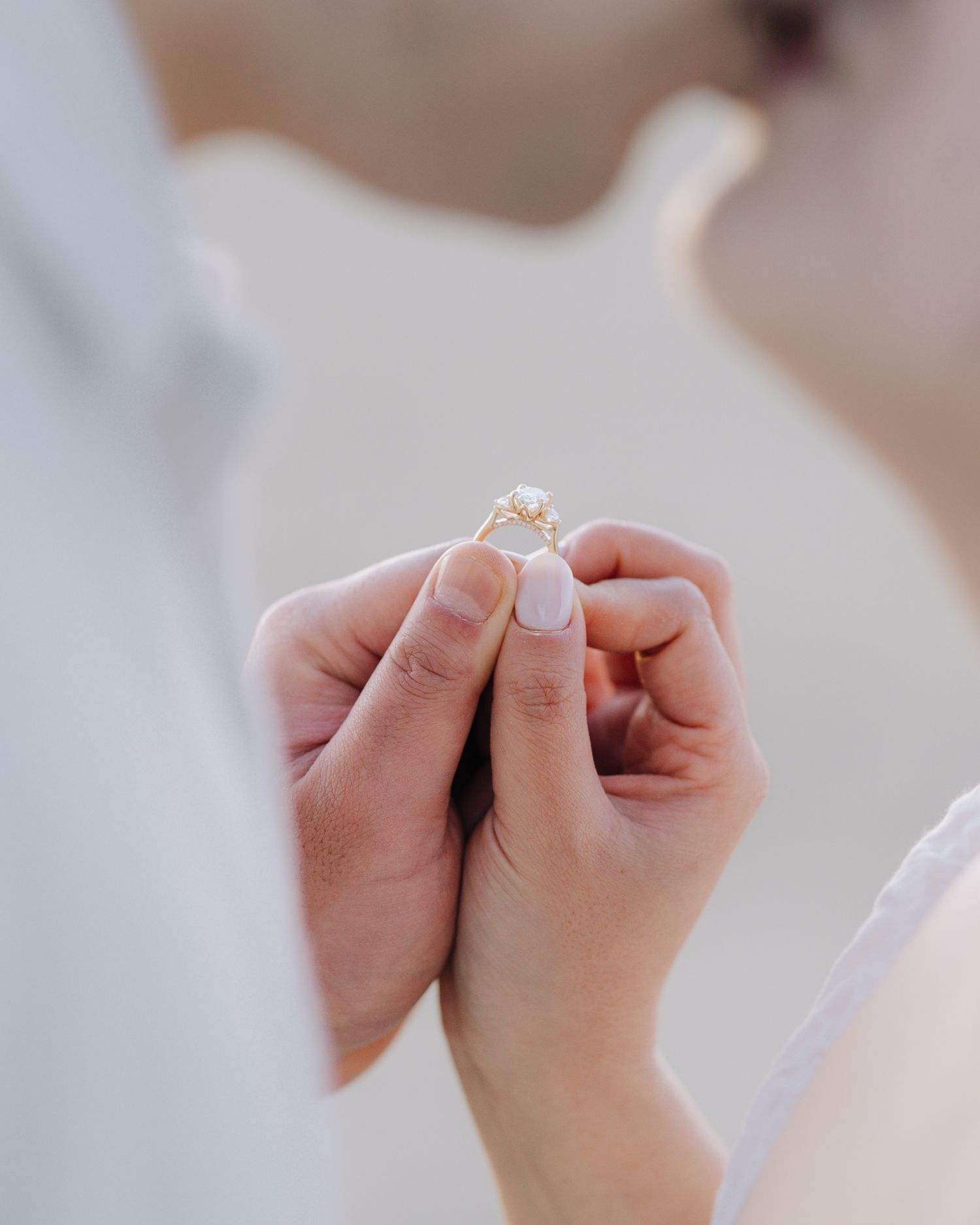 Close-up of couple holding a delicate gold engagement ring with solitaire diamond during beach ceremony in San Francisco, CA.