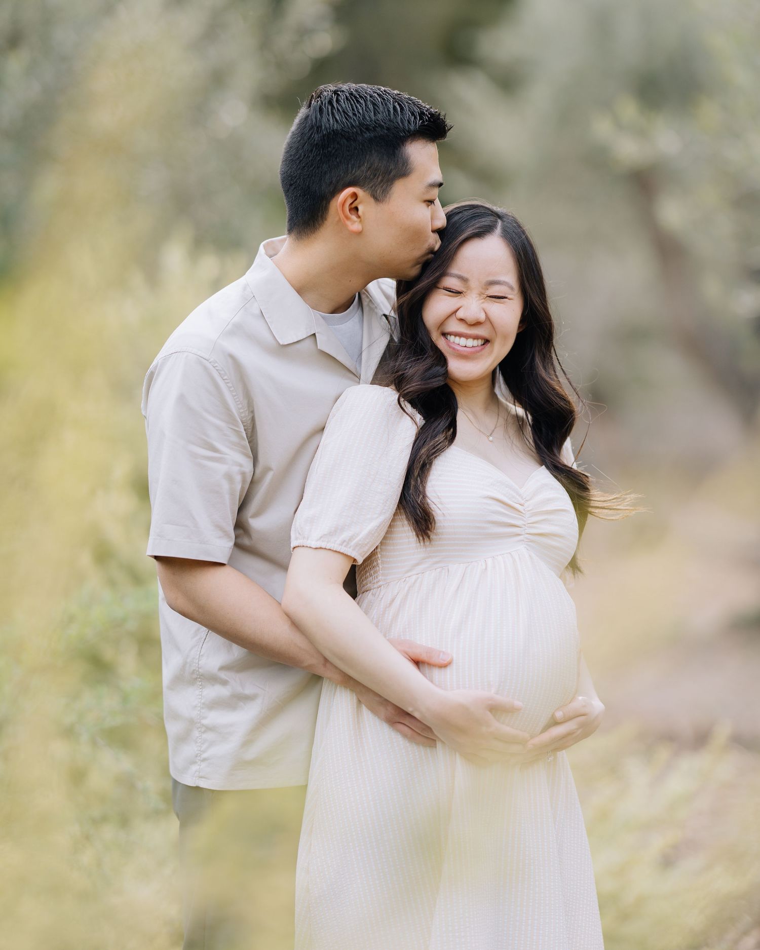 Man kissing pregnant woman on the cheek as she smiles joyfully in a soft outdoor natural setting at Filoli Woodside maternity photoshoot.