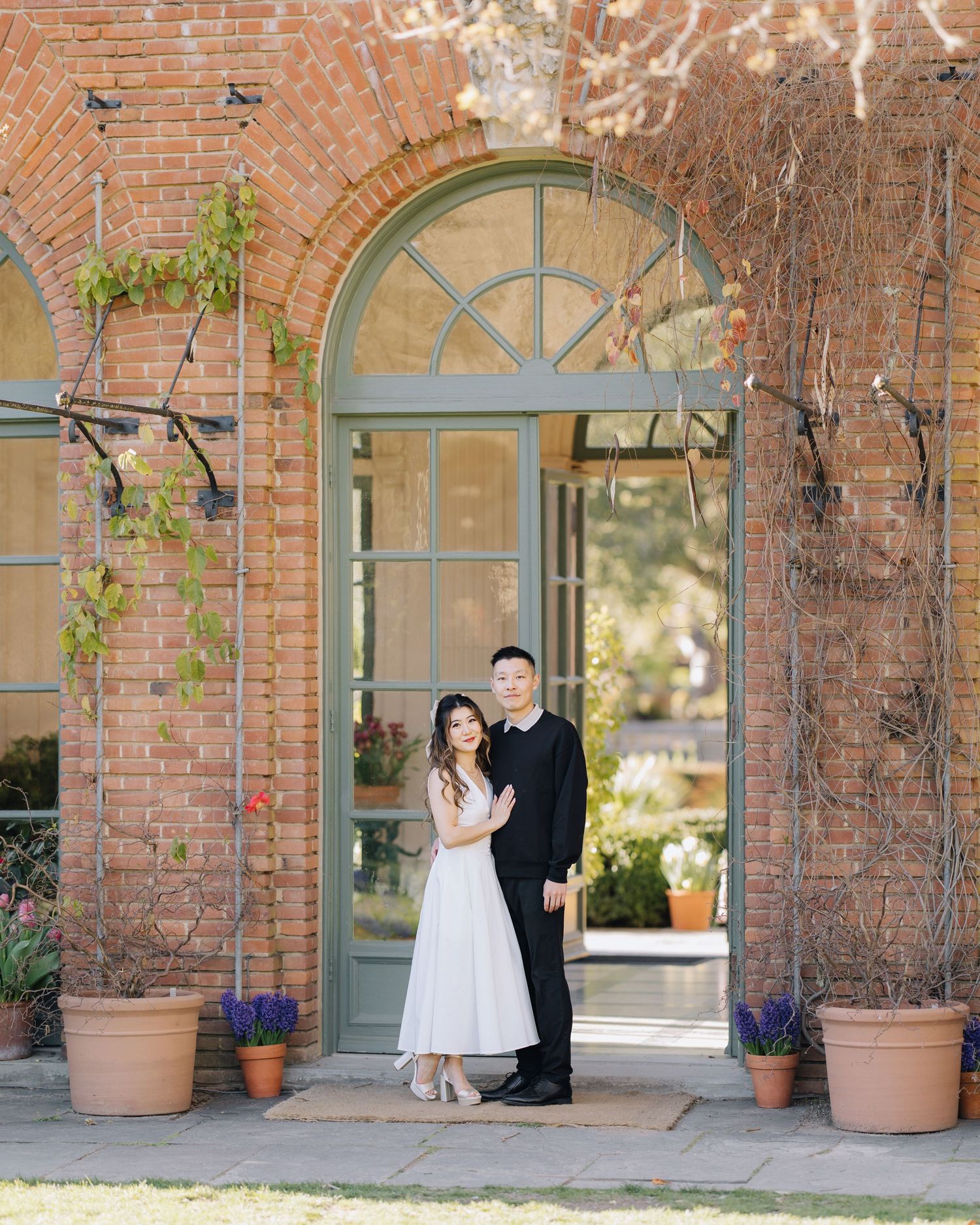 Couple poses in arched doorway of brick building during engagement photo session at Filoli Woodside CA.