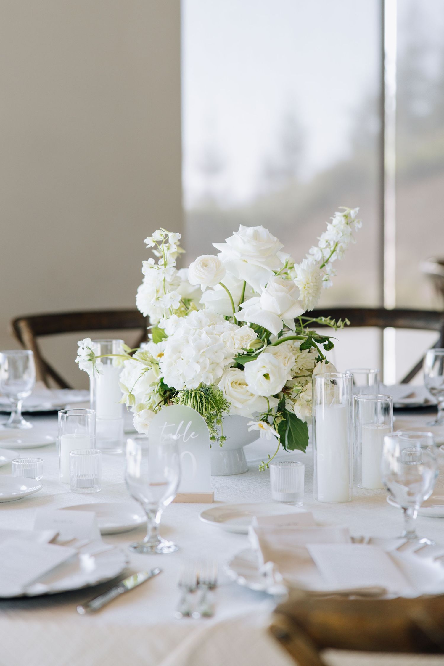 White floral centerpiece with roses and candles on elegantly set wedding reception table in Bay Area.