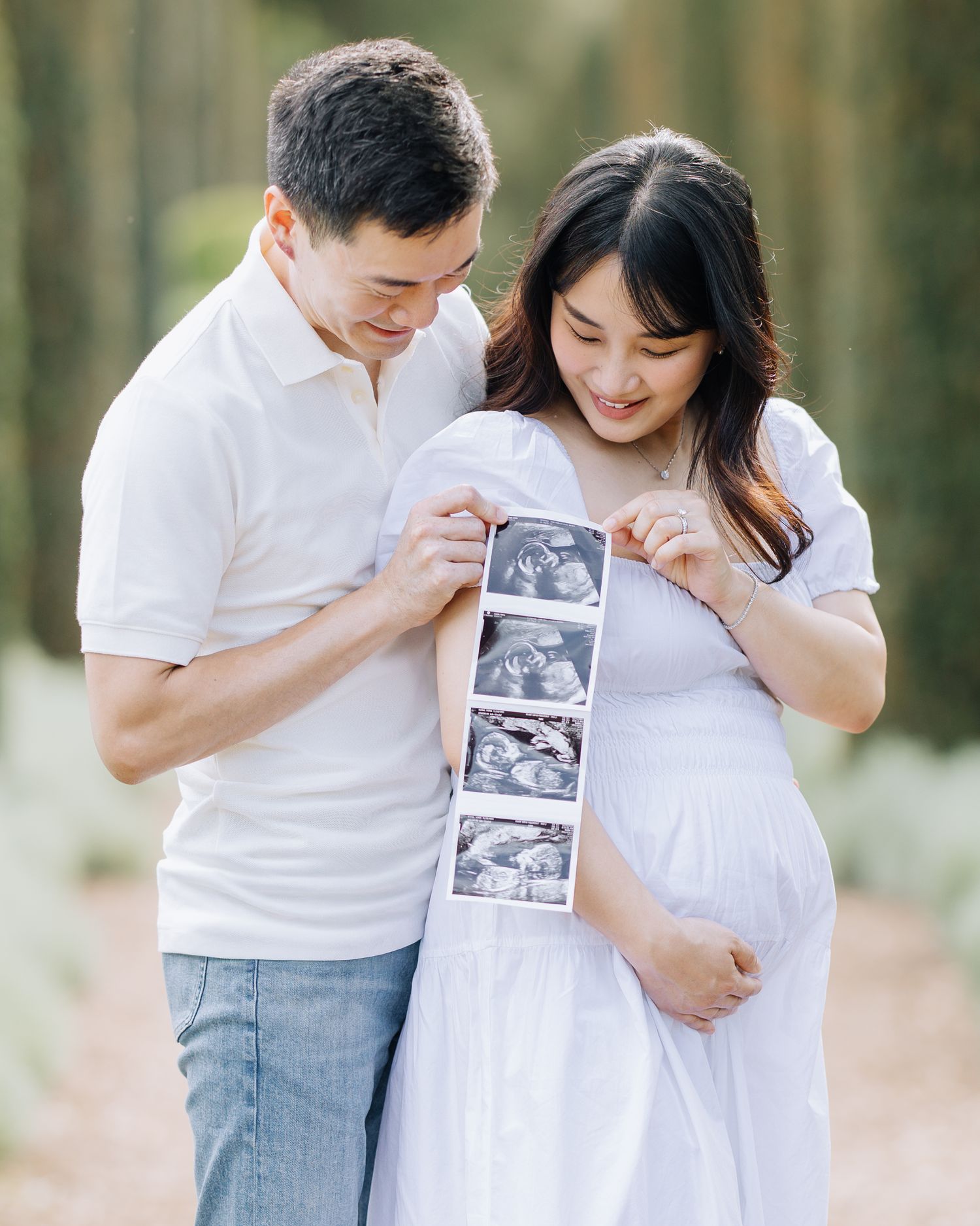 Expecting Asian couple smiling at ultrasound photos during outdoor maternity shoot at Filoli Woodside.
