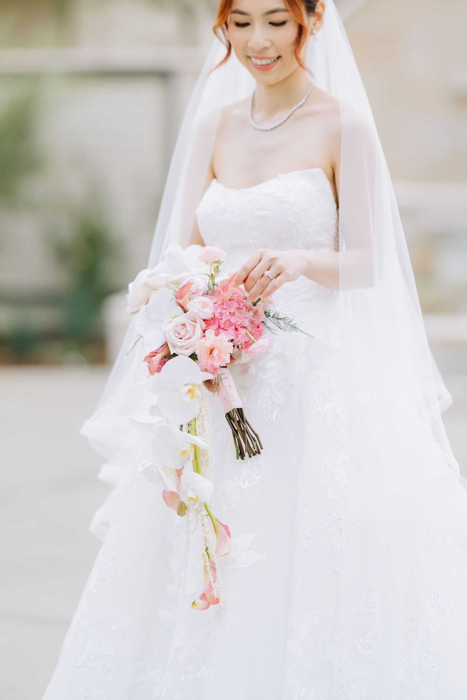 Smiling bride in strapless white gown holding cascading pink and white floral bouquet with veil in Bay Area wedding.