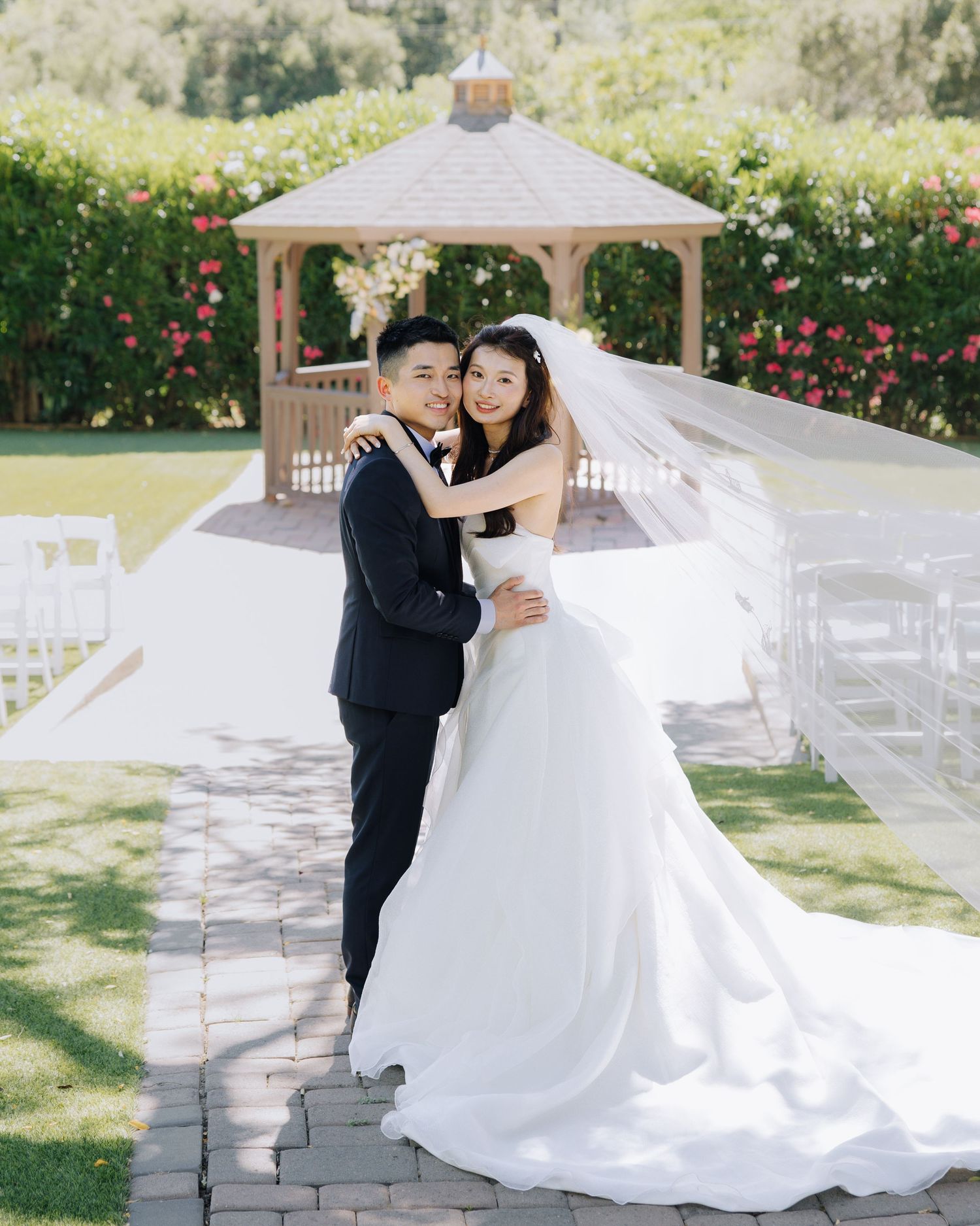 Asian bride and groom pose together in front of a garden gazebo at Elliston Vineyards in Sunol, California.