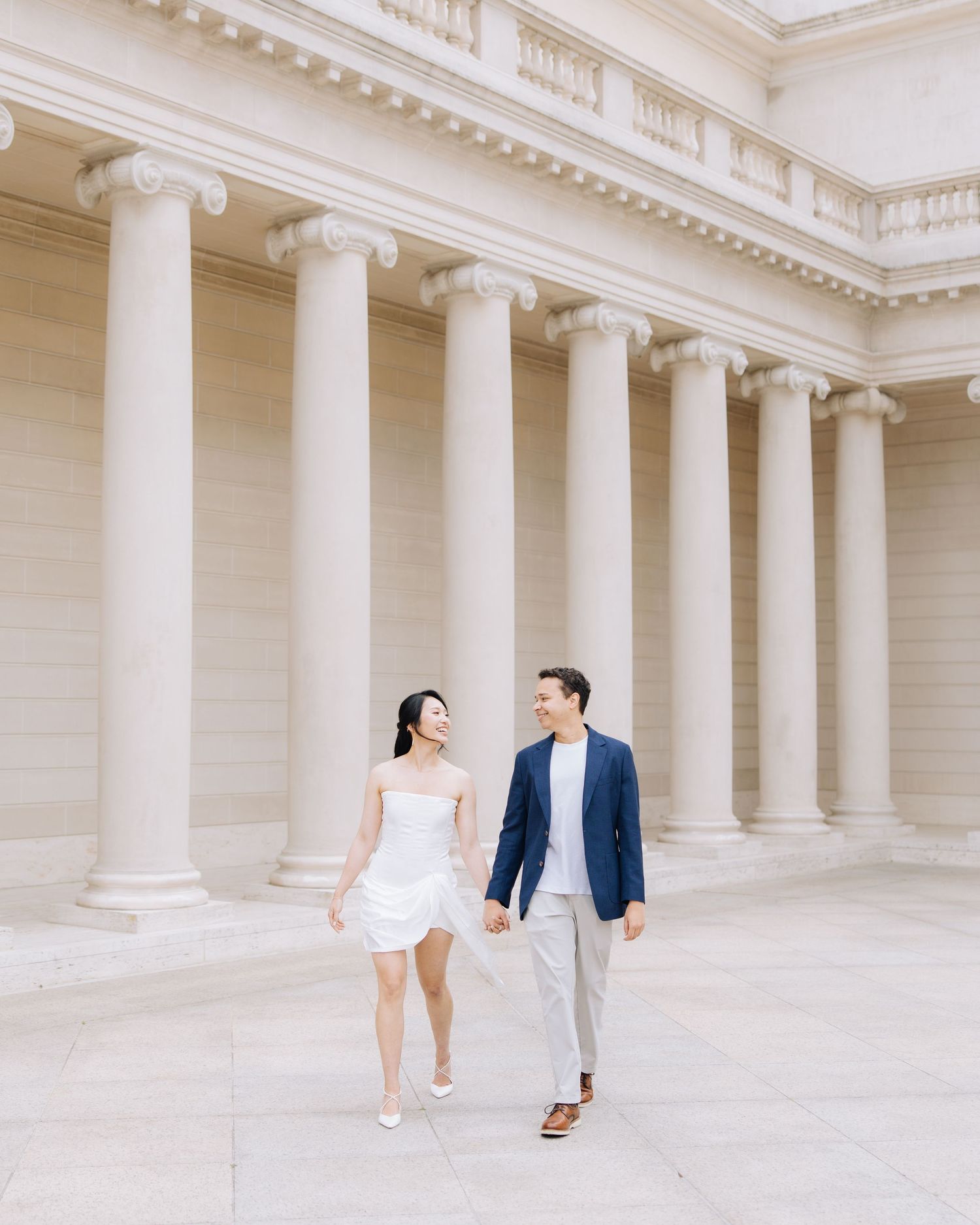 Smiling couple walking hand in hand during engagement photoshoot at Legion of Honor museum in SF.