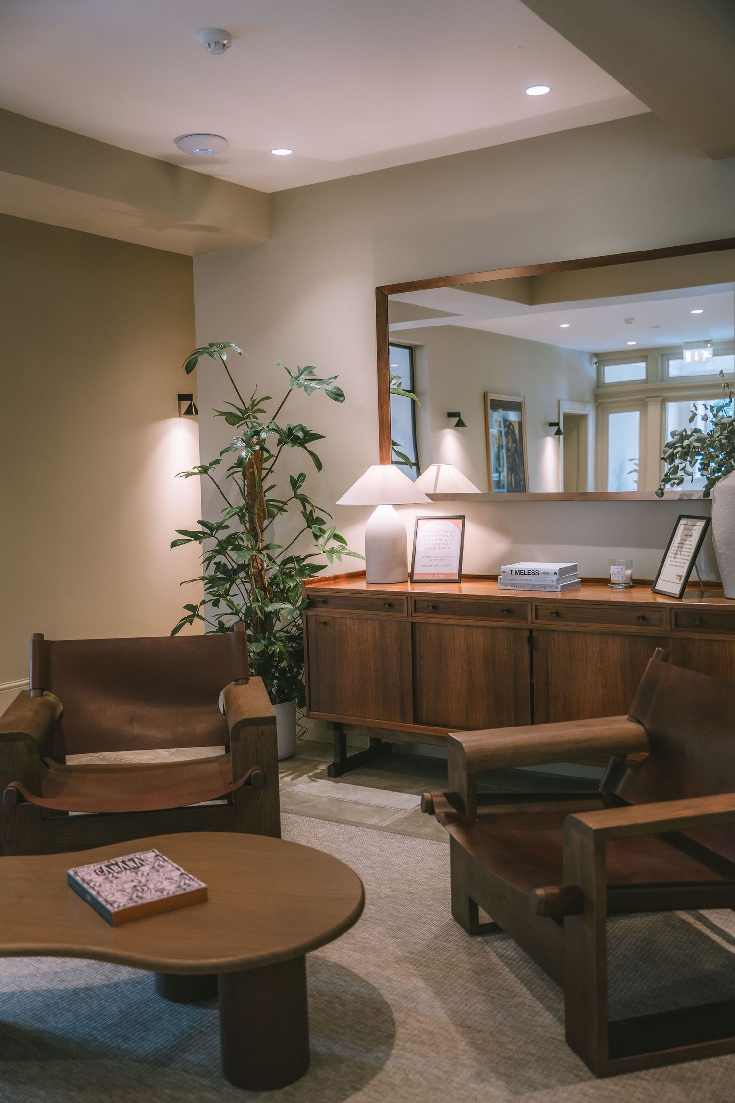 Warm cozy hotel lounge with leather armchairs, round coffee table, wooden sideboard and large mirror.
